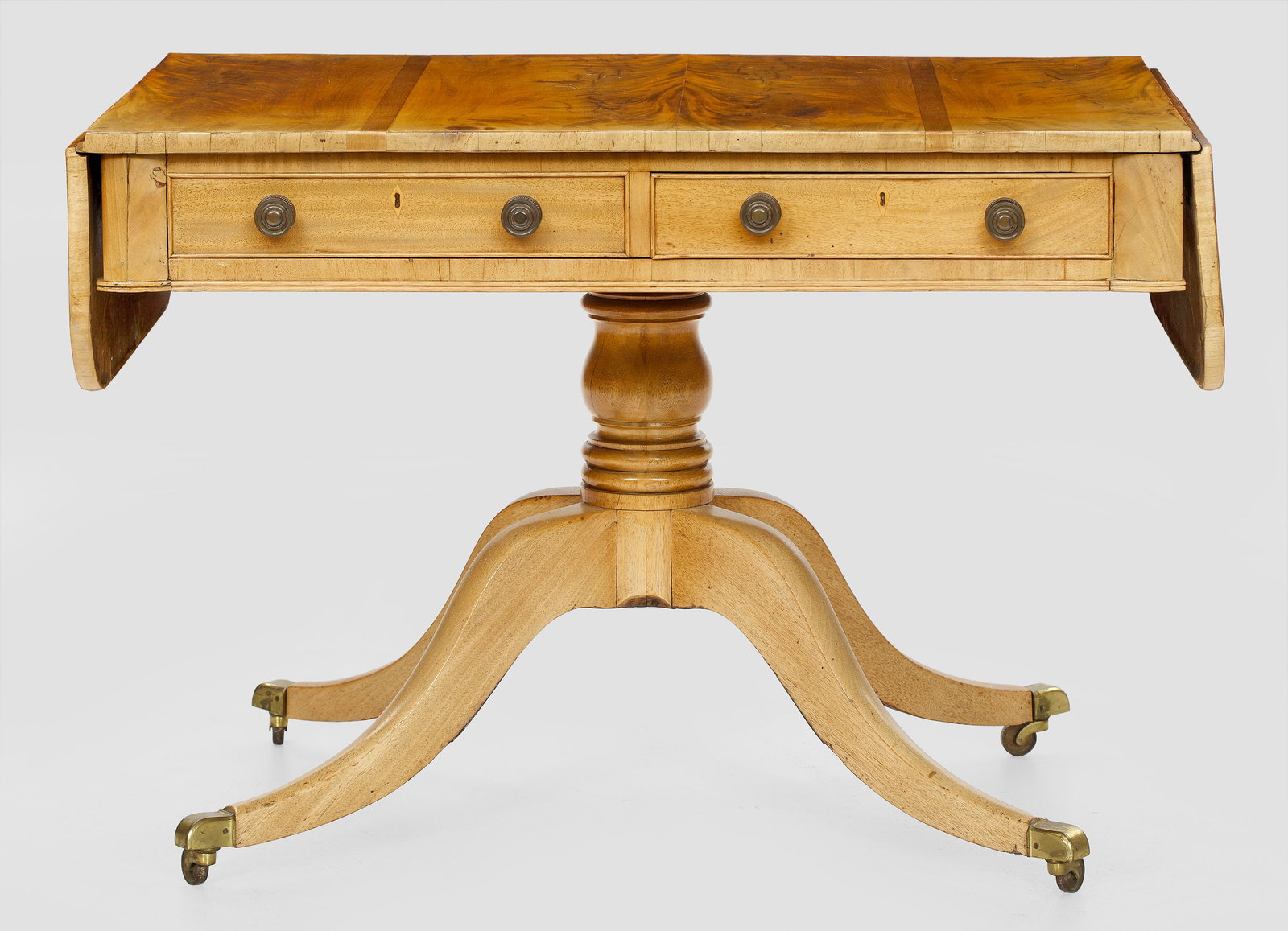 Regency-Tisch: Mahagoni, furniert. Gerader, zweischübiger Zargenkasten auf mehrfach gegliedertem Schaft und geschwungenen Beinen mit Rollen. Rückseitig Blendschubladen. gering überstehende, seitlich aufstellbare