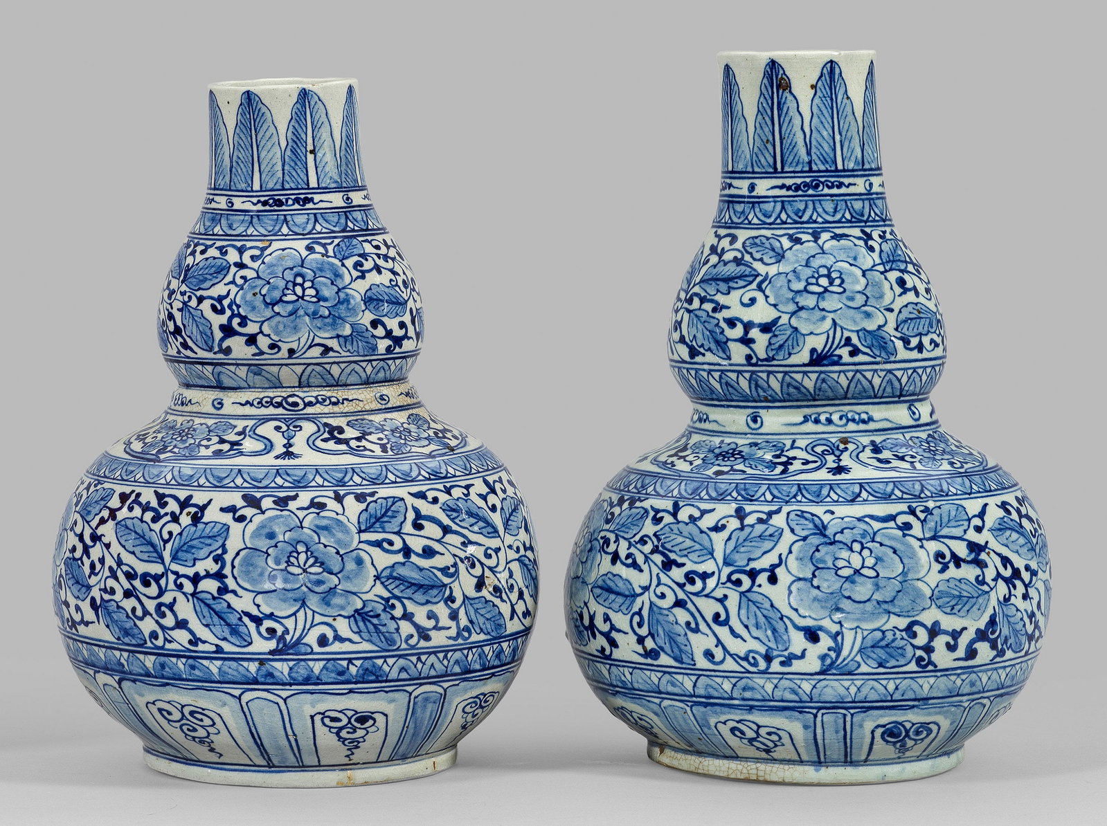 Paar große Vasen mit Blumendekor: Weißgrauer, porzellanartiger Scherben mit Eiseneinschlüssen. Kalebasse- bzw. Doppelkürbisform. Umlaufend dichter floraler und ornamentaler Dekor in unterglasurblauer Malerei. Glasurkrakelee. Minim.
