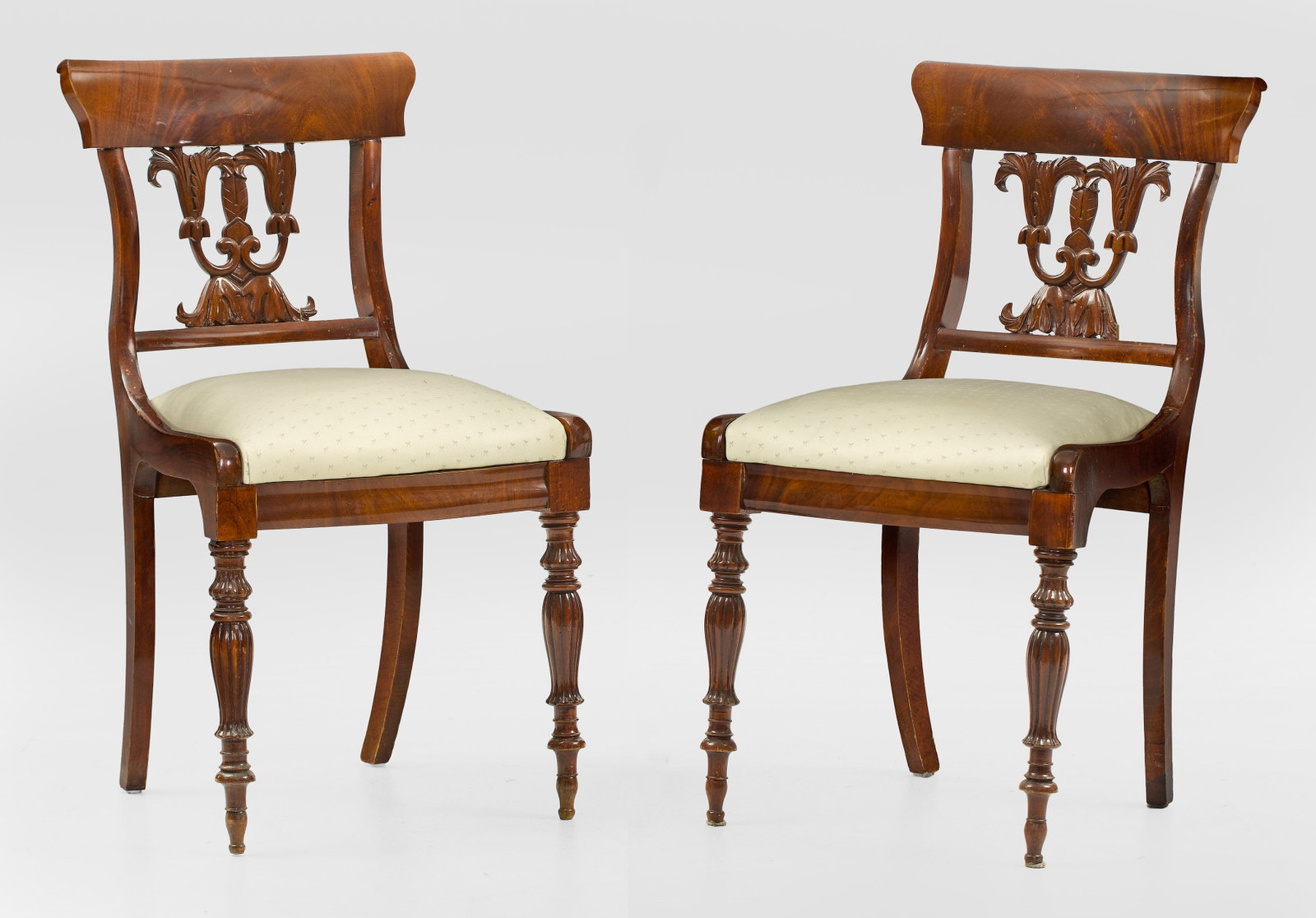Paar Spätbiedermeier-Stühle: Mahagoni, massiv und furniert. Trapezförmige Zarge auf godronierten Balusterbeinen. Durchbrochen gearbeitete Rückenlehnenrahmung mit blattreliefiertem Mittelsteg und breitem oberen Abschluss. Sitzfl