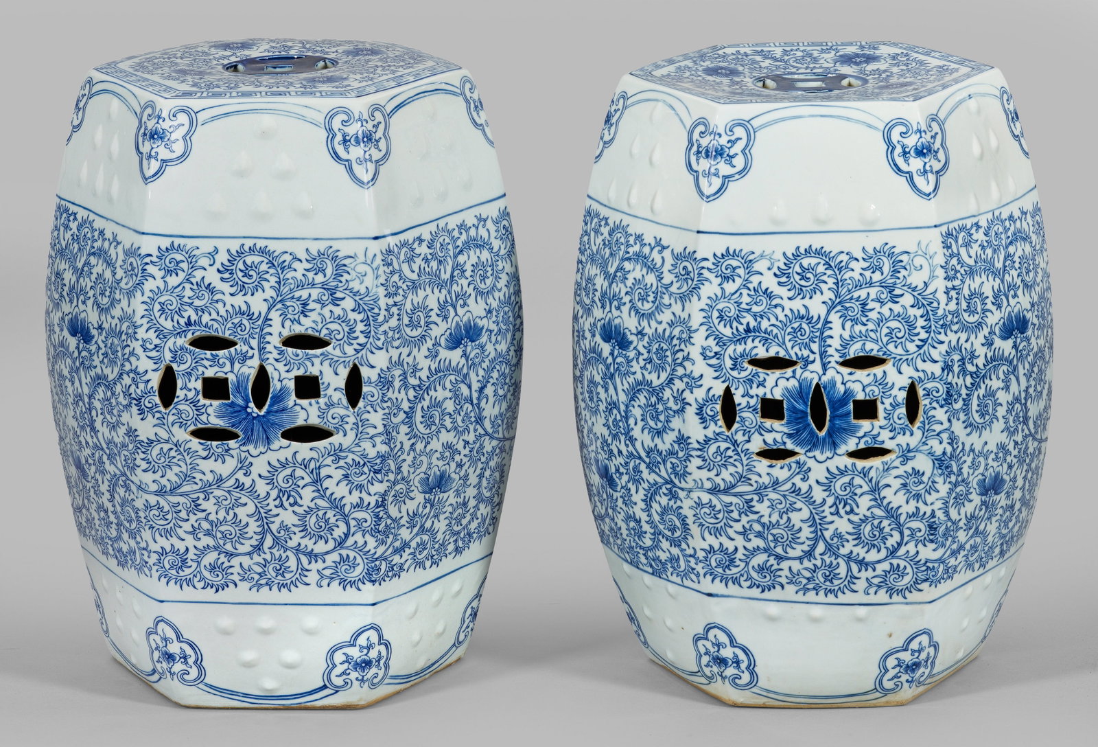 Paar chinesische Blauweiß-Sitzhocker: Porzellan, graustichiger Scherben. Tonnenförmiger, polygonal gekanteter teilw. durchbrochen gearbeiteter Korpus. Umlaufend unterglasurblauer Lotusdekor aus Ranken und Blüten. H. 46,5 cm. A pair of