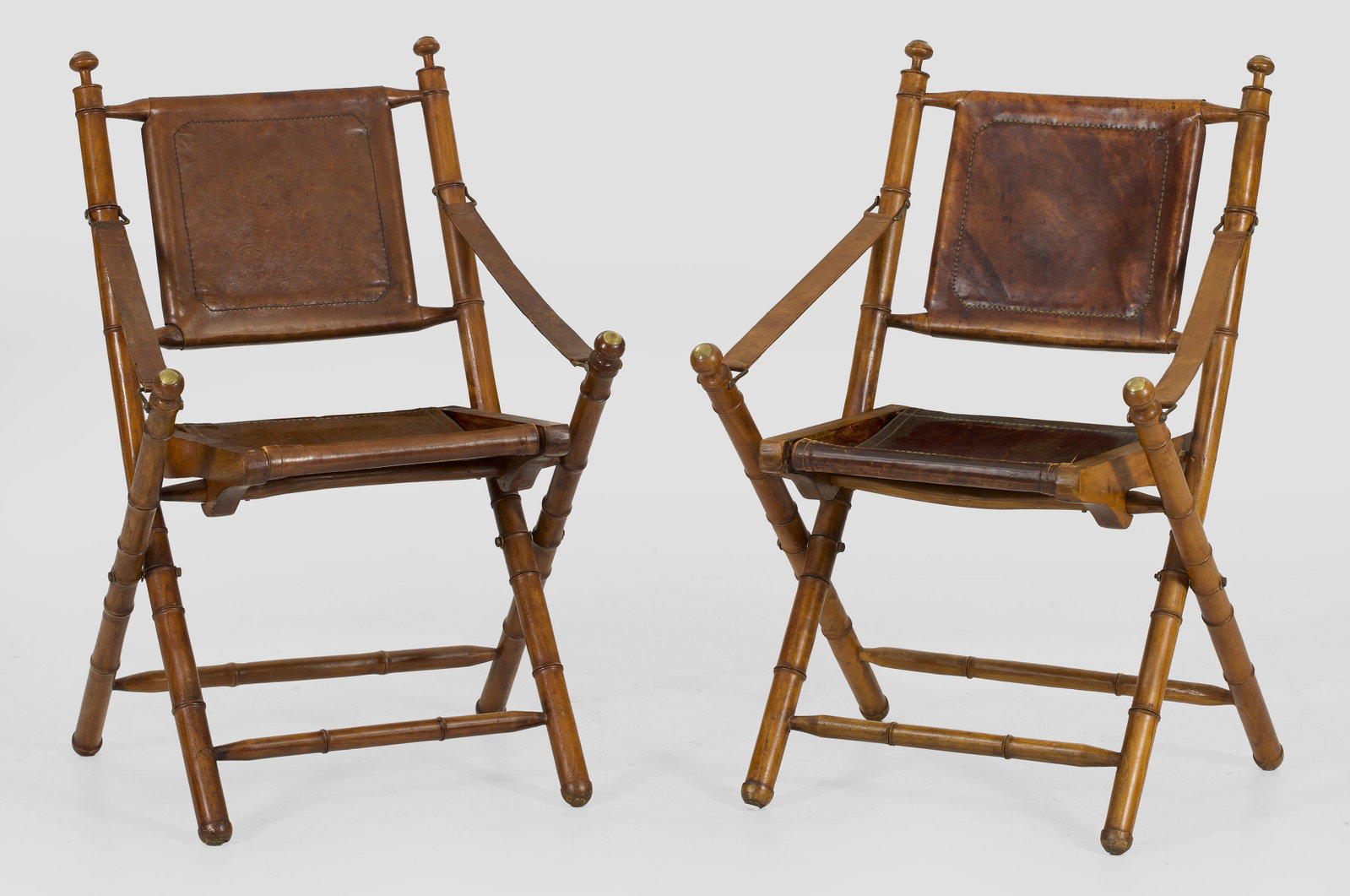 Paar Faltstühle: Holz, in sog. Fauxbamboo-Optik. Faltbares Gestell aus schräggestellten, gegliederten Balusterstäben. Gerade Sitz- und Lehnenfläche aus braunem Leder. Sitz-H. 48 cm. A pair of folding chairs.