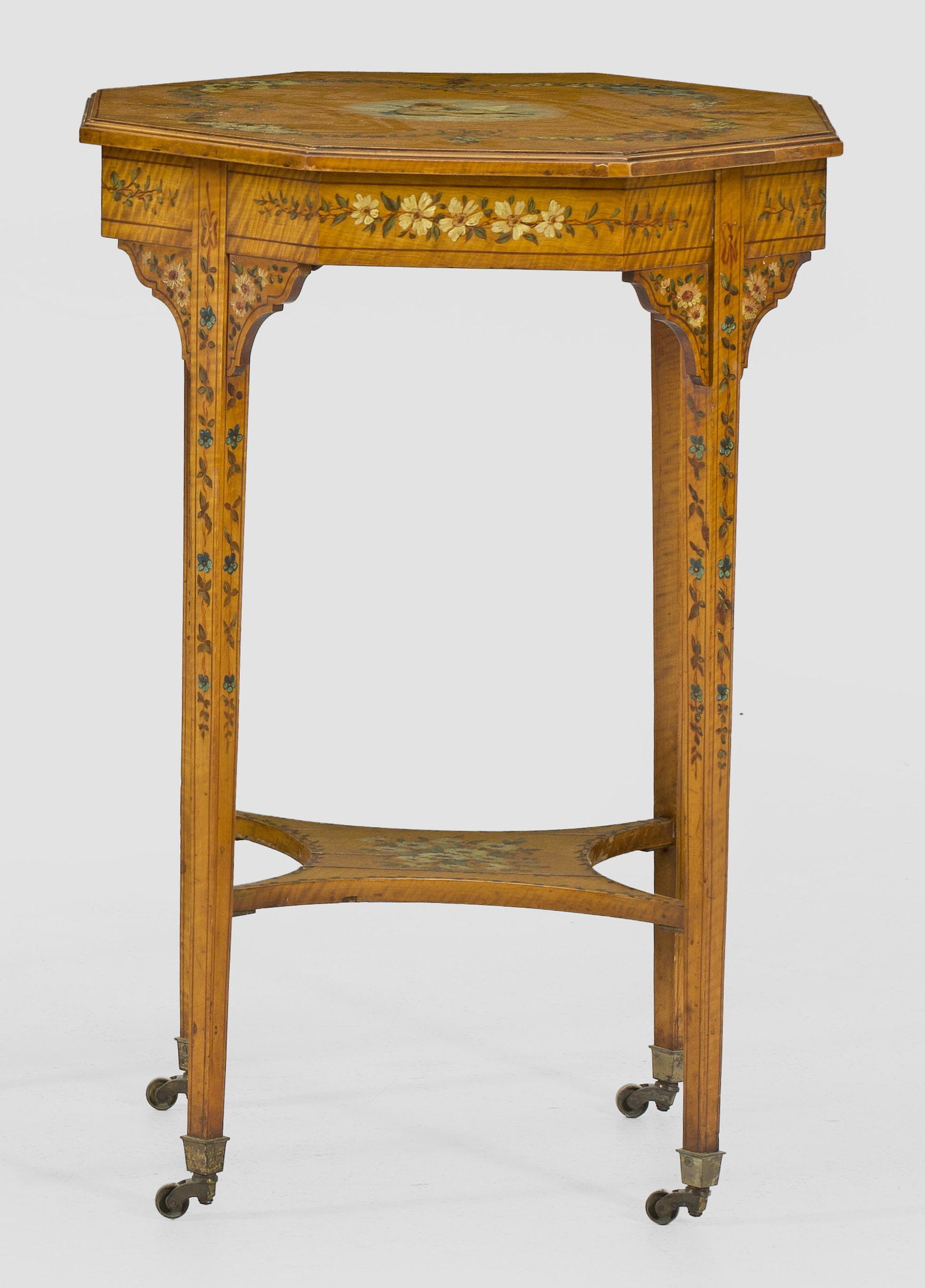 Edwardianischer Beistelltisch: Satinholz, furniert sowie farbig bemalt. Oktogonale Zarge auf schlanken, konischen Vierkantbeinen mit Rollen, unterhalb durch konkav eingezogenes Ablagefach verbunden. Korrespondierende, gering übers
