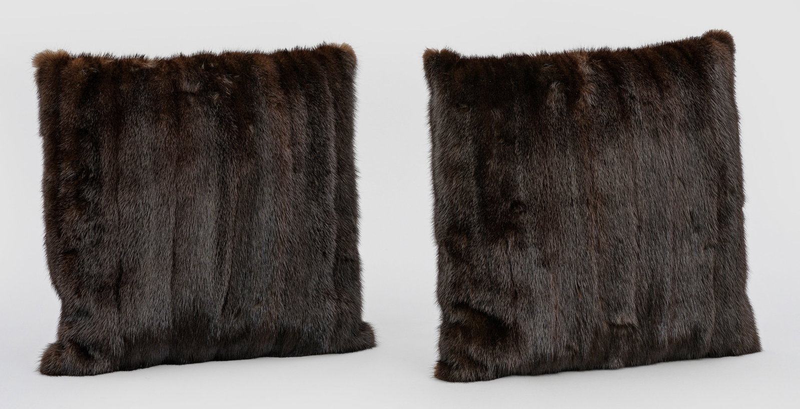 Paar Pelzkissen: Quadratische Kissen aus in Bahnen angeordnetem, schwarzbraunem Nerz in ausgelassener Verarbeitung. Rückseiten aus anthrazitfarbenem Wollkaschmere. Inlett. Ca. 38 cm x 38 cm. A pair of mink fur and wo
