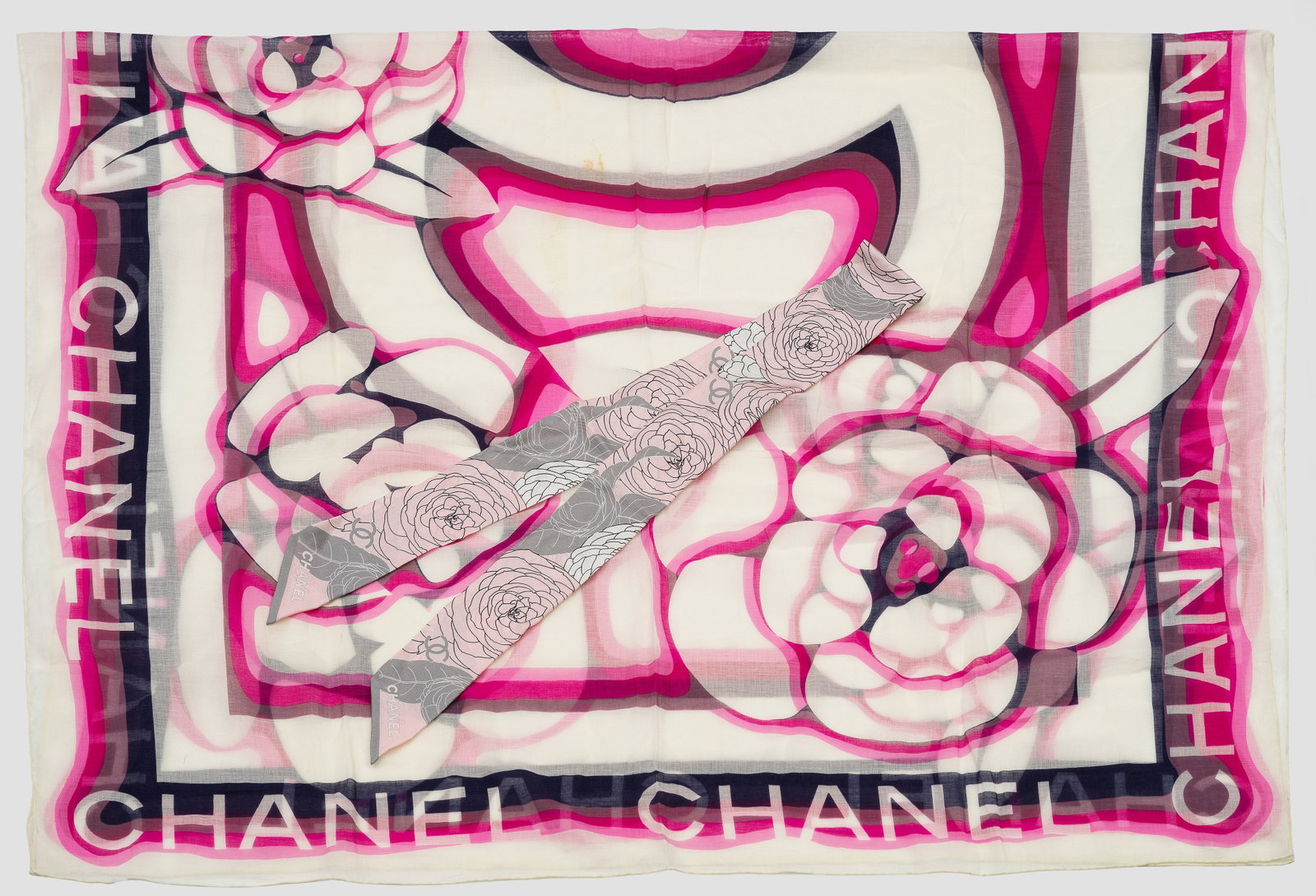 Großes Vintage-Tuch und Halsbinde von CHANEL: Baumwolle und Seide. Blütenmuster und Firmenlogo in Schwarz, Weiß, Grau und Schattierungen von Pink. Halsbinde mit Futteral. Herstellerzeichen. Gebrauchsspuren, kleine Fehlstelle am Rand. 158 cm x 9