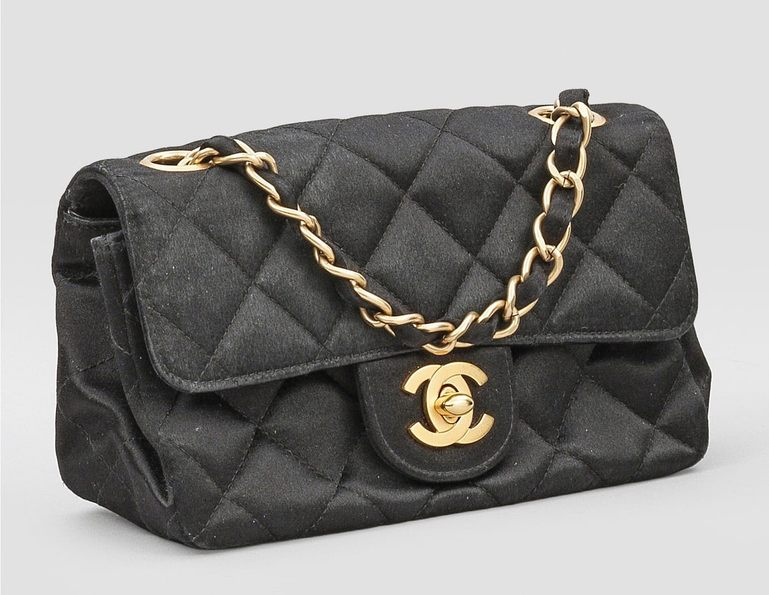 "Timeless Flap Bag" von CHANEL: Schwarzes Satin bzw. Leder in charakteristischer Rautensteppung und vergoldete Hardware. Rechteckiger leicht konischer Korpus mit CC-Logo Drehverschluss. Innenfach mit Seitenfach sowie variable mit Sa