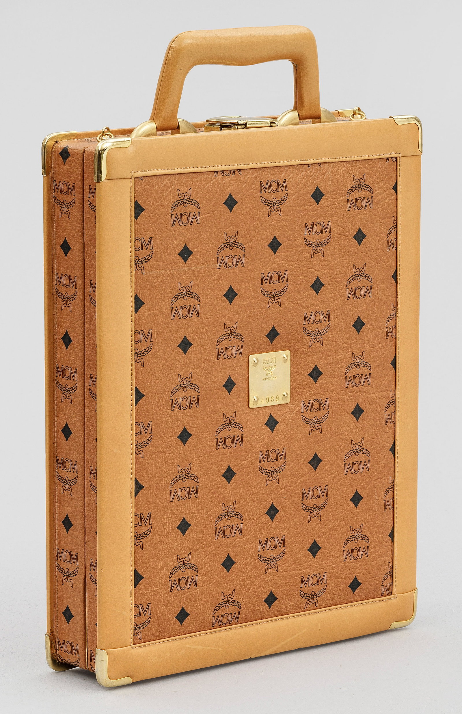 Kleiner Vintage-Koffer von MCM: Cremefarbenes Canvas mit MCM-Logo und konturiertem Lederbesatz sowie goldfarbener Hardware. Rechteckiger Korpus mit abgeschrägtem Griff. Innen Aktenfach mit Nebenfächern. Herstellerzeichen. Nr. 4989