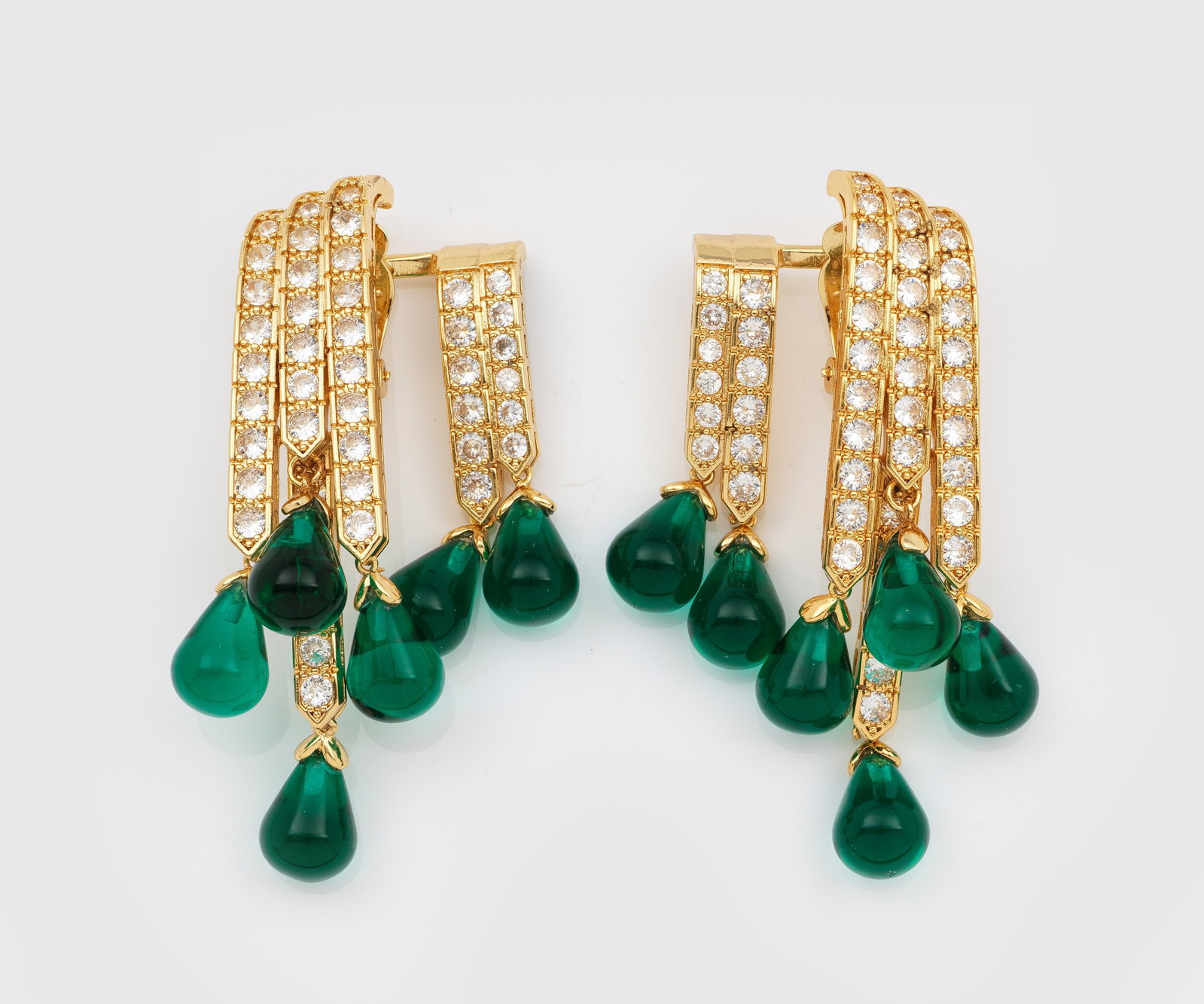 Paar glamouröse Vintage-Ohrclips: Metall, vergoldet. Zweigeteilte Clips aus gebogten Streben mit Strassbesatz sowie gestaffelt angeordneten Tropfen aus grünem Glas. L. 7 cm. A pair of gilt metal Vintage ear clips.