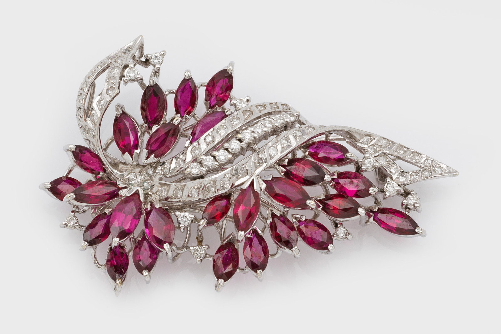 Demi Parure mit Burma-Rubinen aus den 1960er Jahren: Weißgold, gest. 12 ct./585. Brosche und korrespondierendes Paar Ohrclips. Schauseitig besetzt mit taubenblutroten Rubinen von zus. ca. 12 ct. und Diamanten von zus. ca. 1,20 ct.; Ges.-Gew. ca. 29,11 