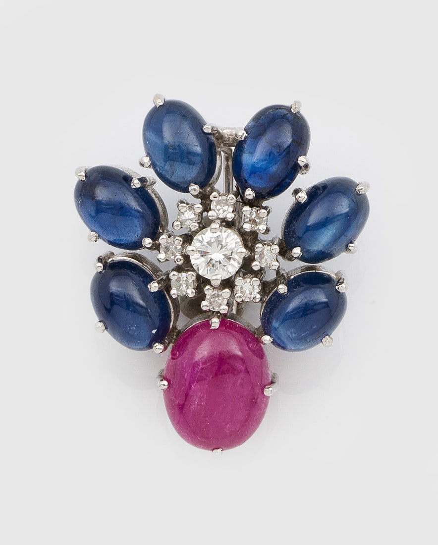 Klassischer Saphir-Rubin-Clip-Anhänger: Weißgold, gest. 585. Schauseitig besetzt mit Saphir- und Rubin-Cabochons sowie Brillanten von zus. ca. 0,30 ct.; Gew. ca. 7,36 g. Clip pendant set with sapphires, rubies and diamonds approx. 0,30ct.,