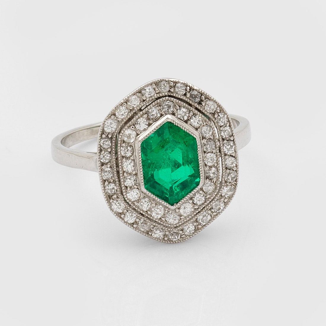 Feiner Art Déco-Smaragd-Diamantring: Platin. Hexagonaler Ringkopf zentral besetzt mit korrespondierendem Smaragd von ca. 0,80 ct., entouriert von kleinen Altschliffdiamanten. Gew. ca. 4,00 g. Ring set with an emerald approx. 0,80 ct. and