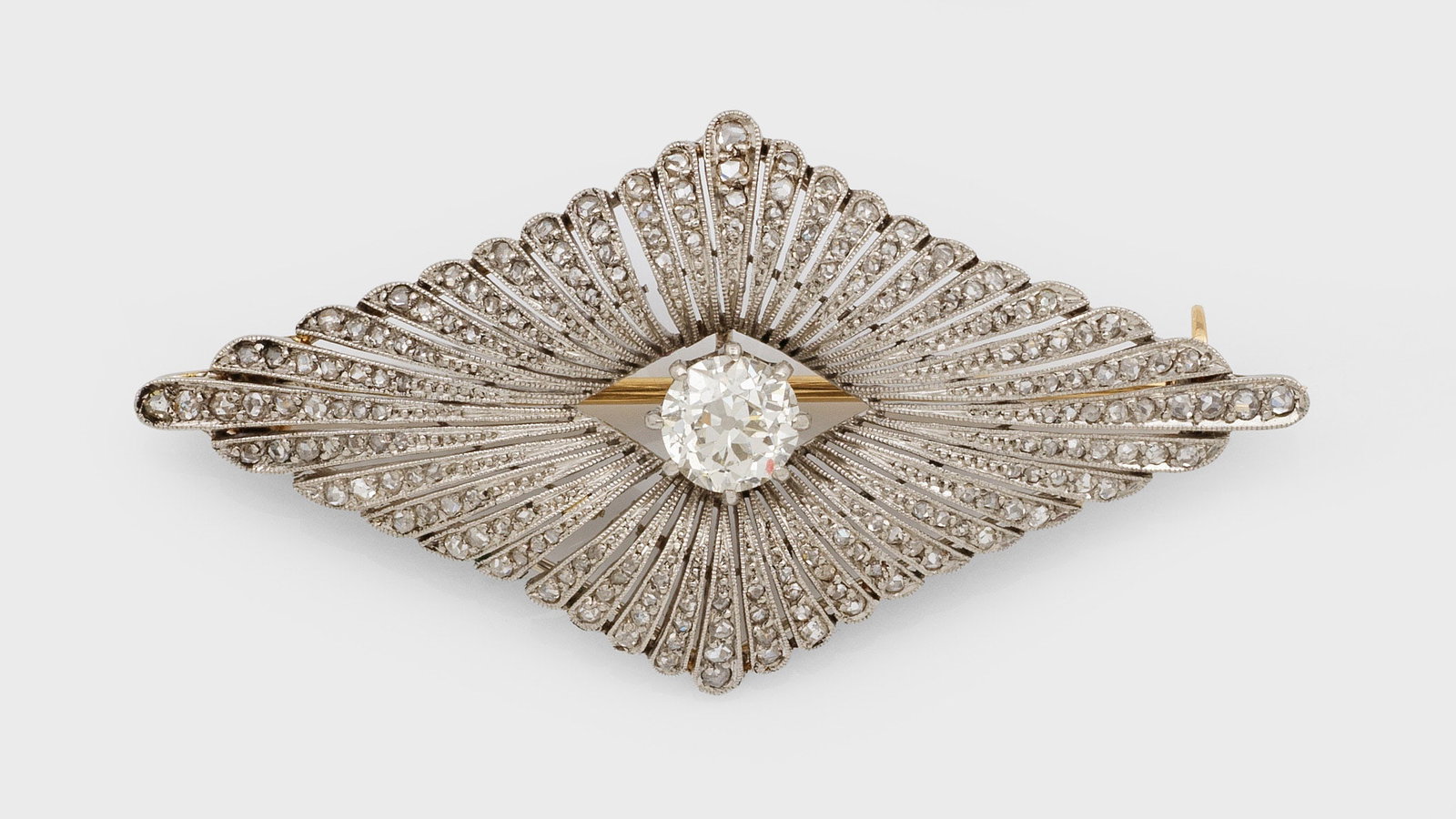 Art Déco-Brosche: Platin. Leicht bombierte Form, zentral besetzt mit einem Altschliffdiamantsolitär von ca. 1,00 ct. (I-J/vs), ausgefasst mit kleinen korrespondierenden Diamanten, umzogen von feinen