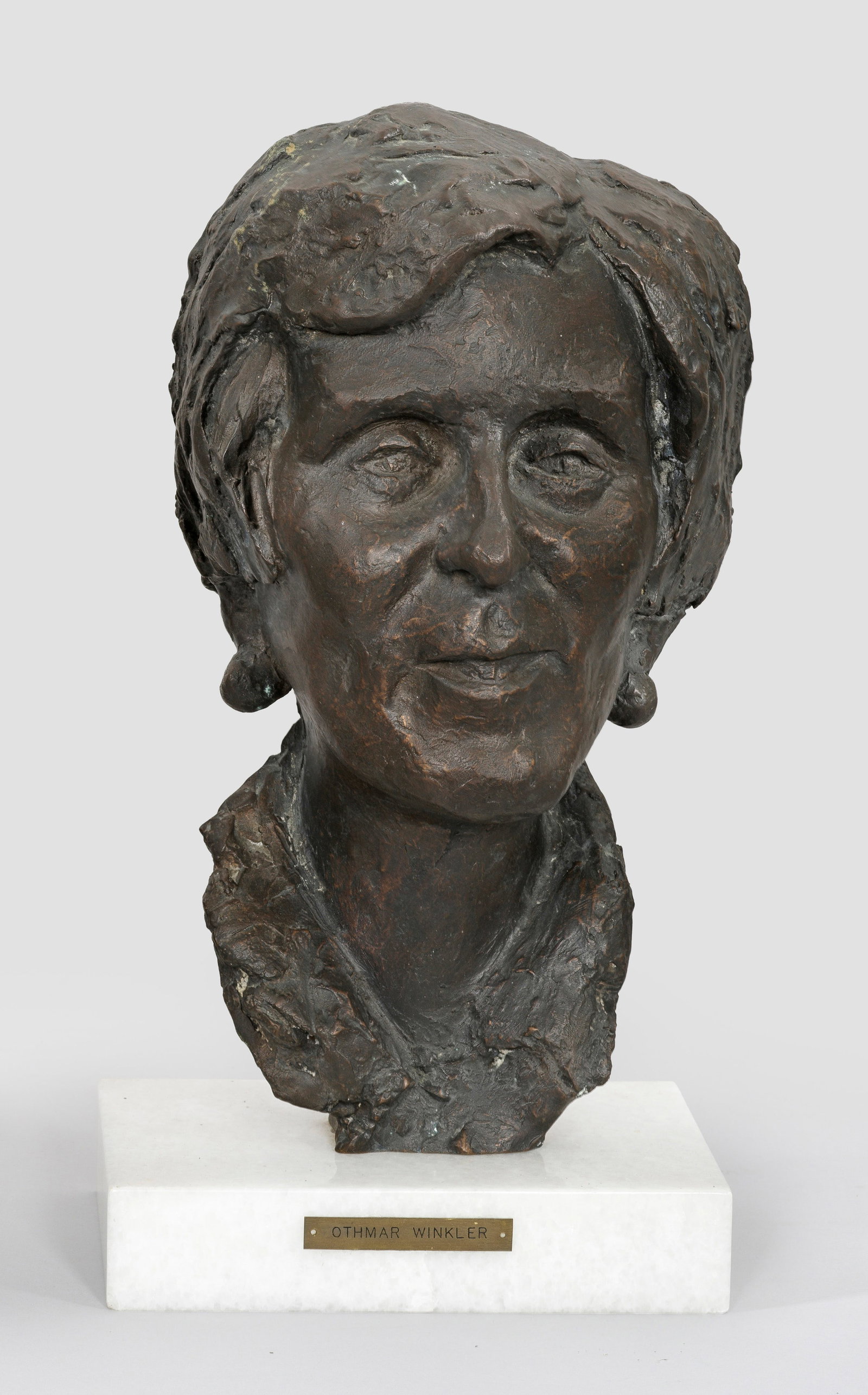 Othmar Winkler: (1907 Bruneck/Südtirol - 1999 Trient) Weiblicher Porträtkopf Bronze, dunkelbraun patiniert, um 1975; Plinthe aus weißem Kunstmarmor, schauseitig Plakette mit Künstler-Bez.; Der bedeutende, von Got