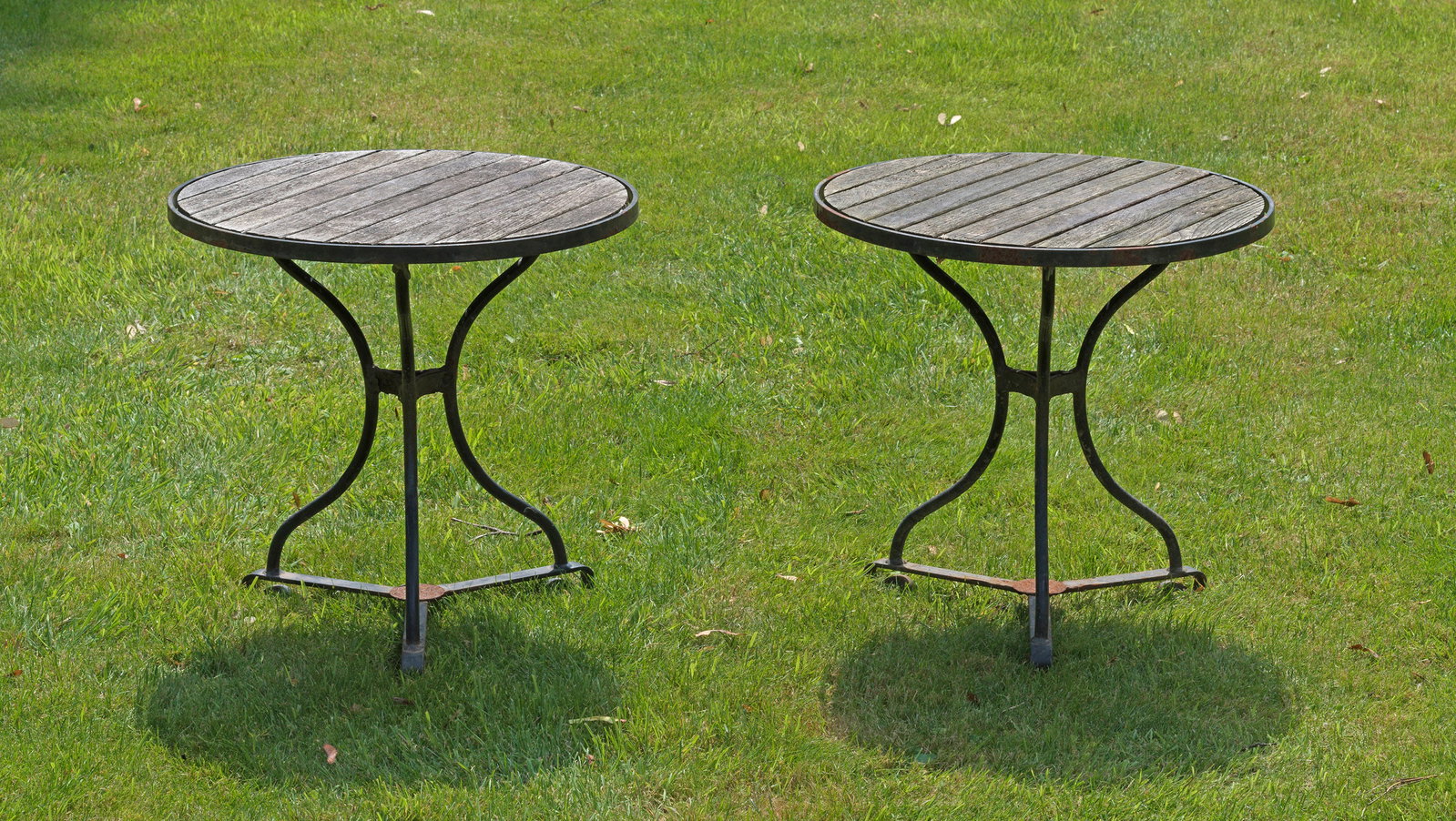 Paar Beistelltische "Fontenay" von Garpa: Plantagenteak und Eisen. Sternförmig geschwungenes, schwarz lackiertes Gestell mit runder durch Streben bebretterter Platte. Witterungsspuren und Patina. H. und D. ca. 55 cm. A pair of German round s