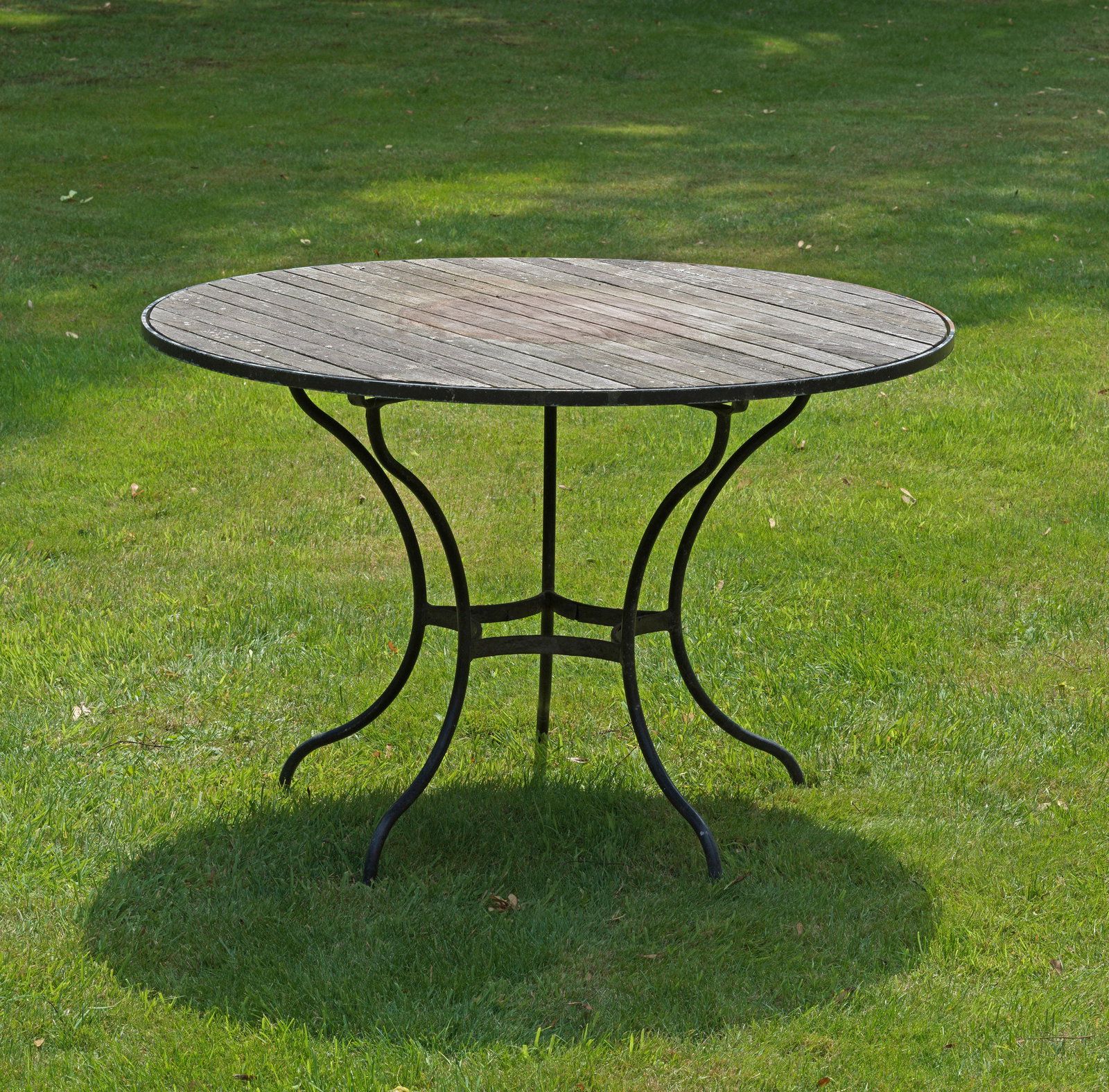 Runder Gartentisch "Fontenay" von Garpa: Plantagenteak und Eisen. Sternförmig geschwungenes, schwarz lackiertes Gestell mit runder durch Streben bebretterter Platte. Witterungsspuren und Patina. H. ca. 75 cm. D. ca. 110 cm. A German round g
