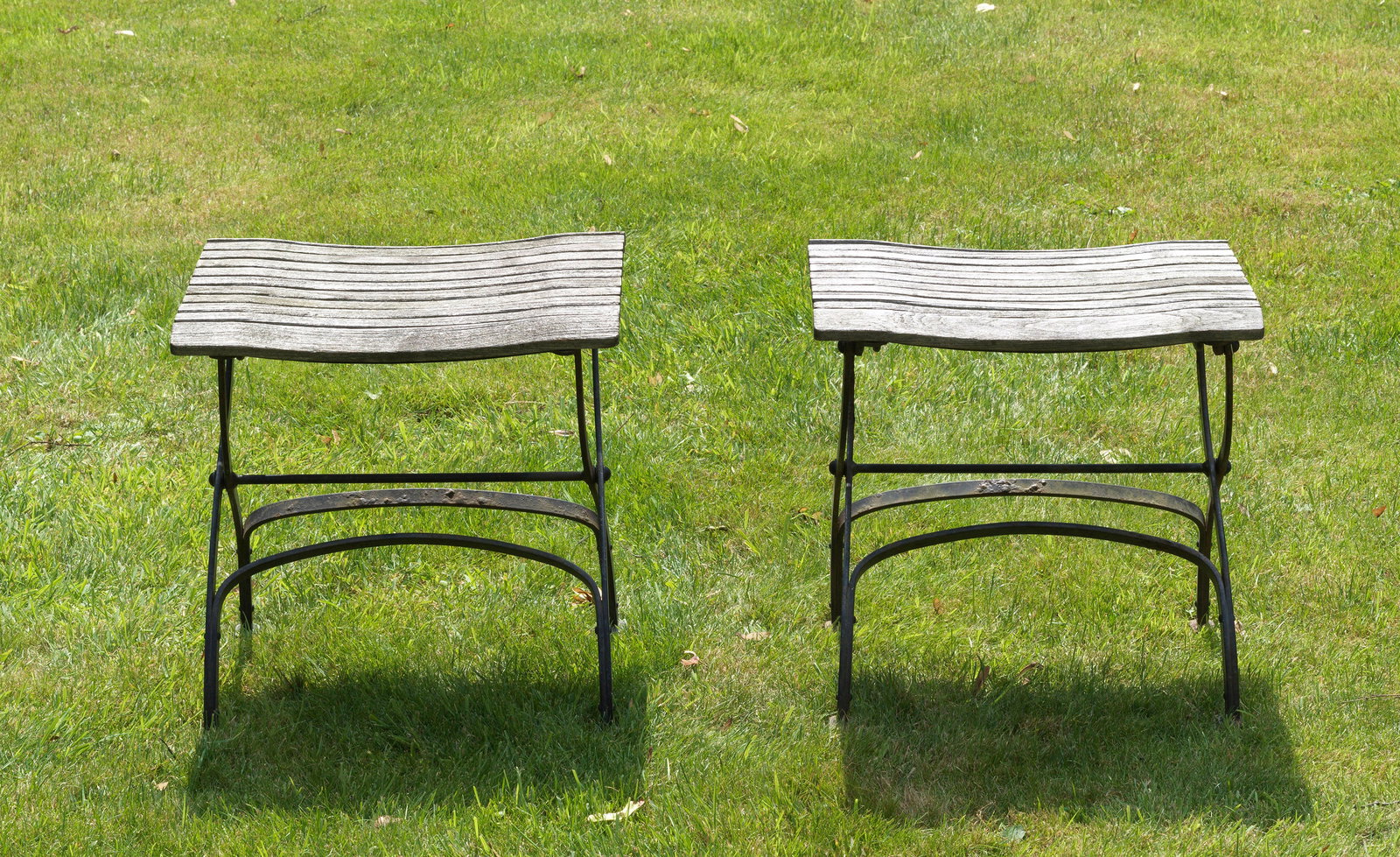 Paar Hocker "Fontenay" von Garpa: Plantagenteak und Eisen. Scherenförmig geschwungenes, schwarz lackiertes Gestell mit rechteckiger durch Streben bebretterter Platte. Witterungsspuren und Patina. H. ca. 47 cm. A pair of German stools