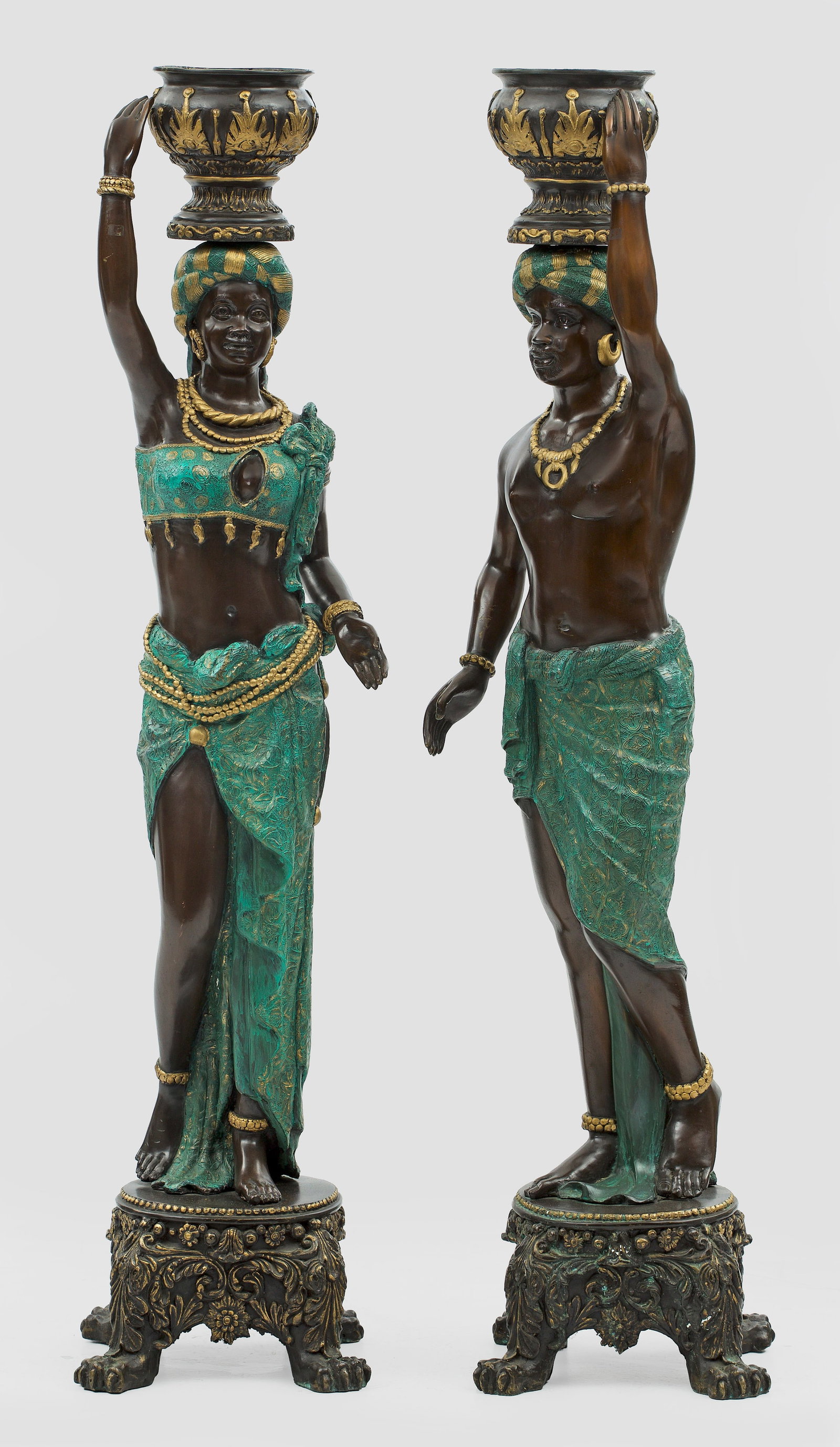 Paar außergewöhnliche Figuren-Jardinièren: Bronze, dunkelbraun patiniert, teilw. türkisfarben bemalt und vergoldet. Über rundem Sockel mit Tatzenfüßen im Kontrapost stehendes, nubisches Figurenpaar, jeweils einen Cachepot auf den Kopf halt