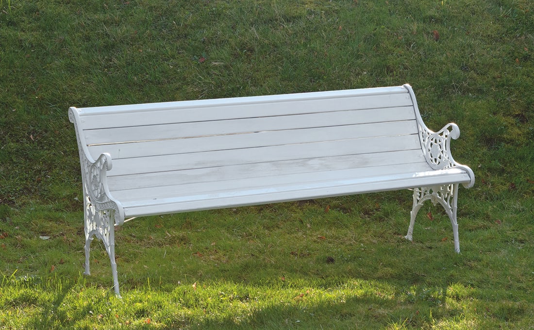 Gartenbank: Metall und Holz, weiß lackiert. Schmale, durchbrochen gearbeitete Seitenwangen aus Volutenmotiven und Rosetten. Geschweifte Sitz- und Lehnenfläche aus dicht angeordneten Stegen. H. 74 cm. 164 cm x 5