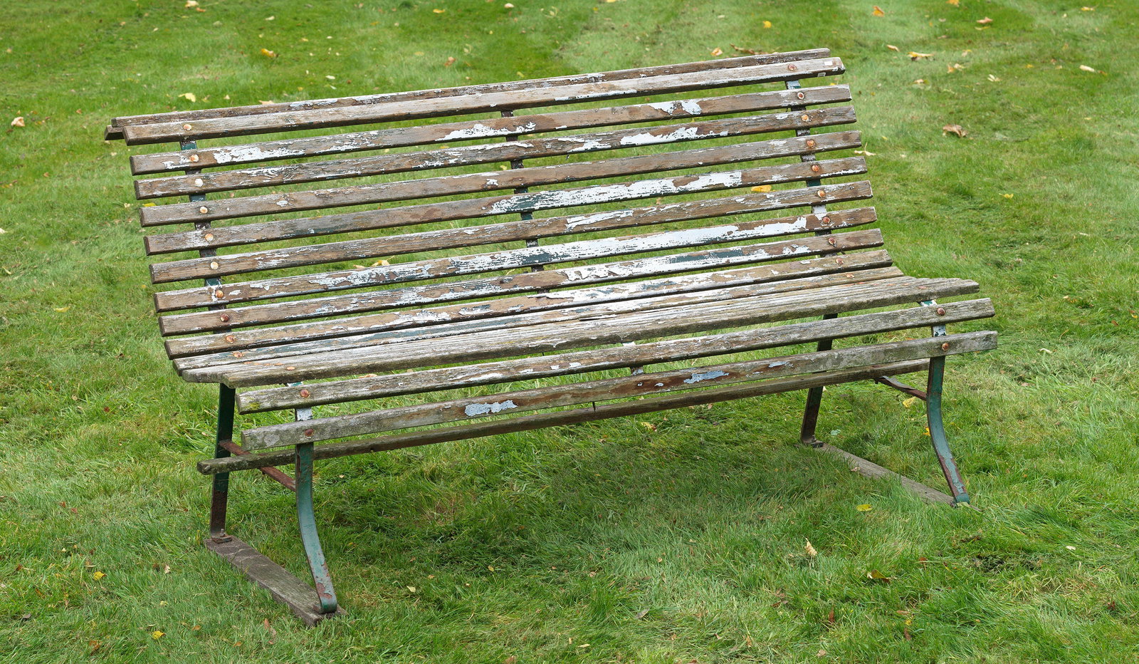 Parkbank: Eisen, lackiert und Holz mit starker Witterungspatina. Durchbrochen gearbeitete Seitenwangen aus schmalen Streben. Geschweifte Sitz- und Lehnenfläche aus dicht angeordneten, gekanteten Stegen. H. 86 