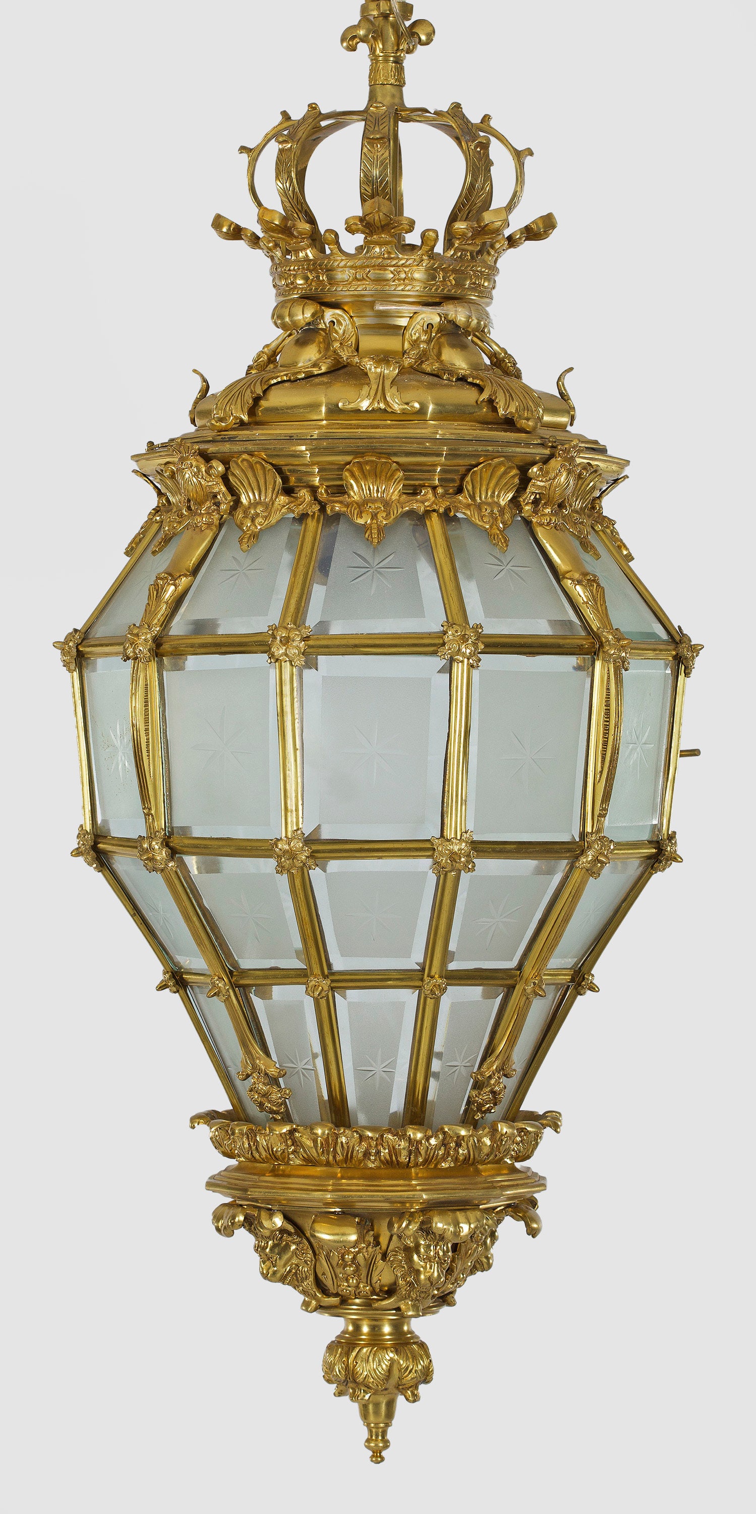 Repräsentative Deckenampel im Louis XIV-Stil: Bronze. Balusterförmiger, gekanteter Korpus aus schmalen Stegen. Reiche Dekorationen aus üppigen Blattkartuschen. Oberer Abschluss in Form einer großen Bügelkrone. Teilw. satinierte Glaseinsätze