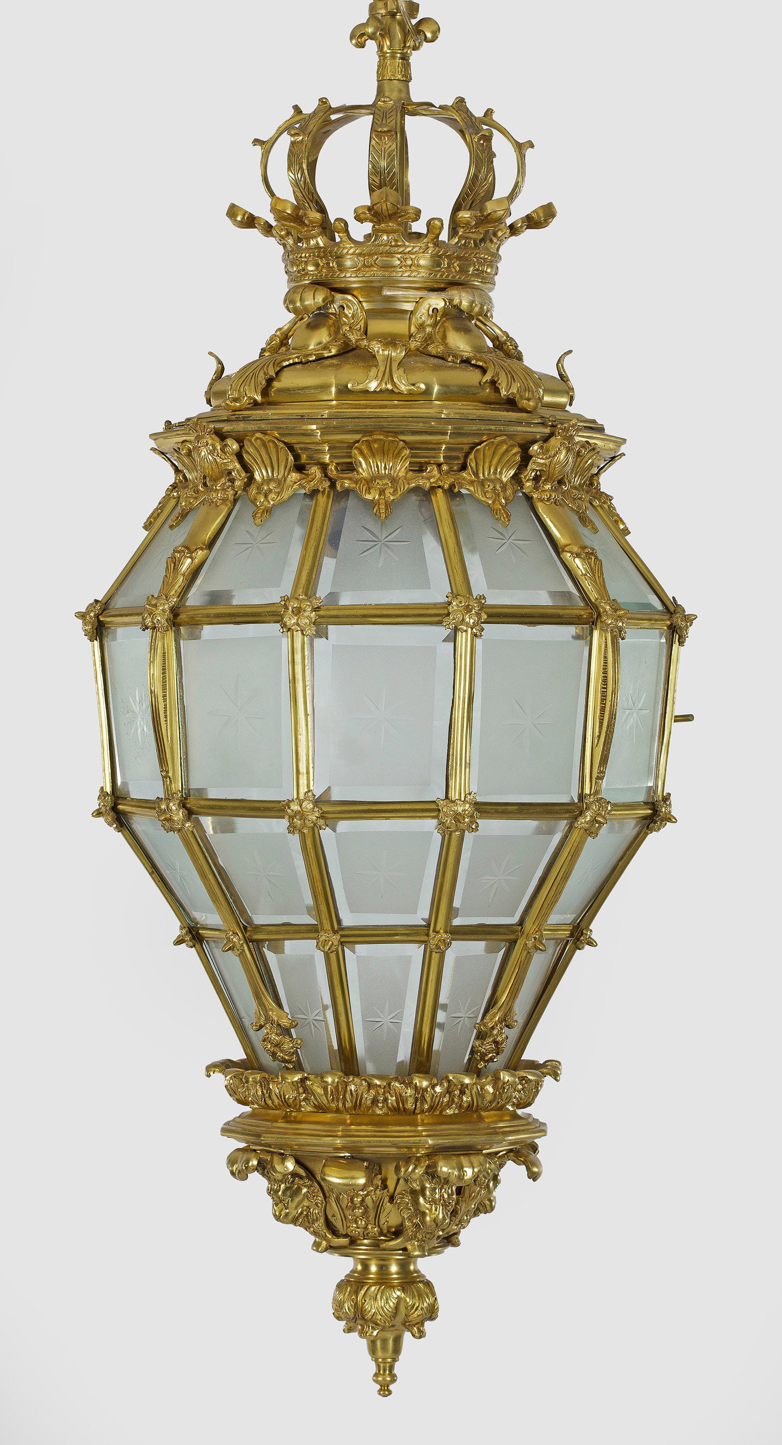 Repräsentative Deckenampel im Louis XIV-Stil: Bronze. Balusterförmiger, gekanteter Korpus aus schmalen Stegen. Reiche Dekorationen aus üppigen Blattkartuschen. Oberer Abschluss in Form einer großen Bügelkrone. Teilw. satinierte Glaseinsätze 