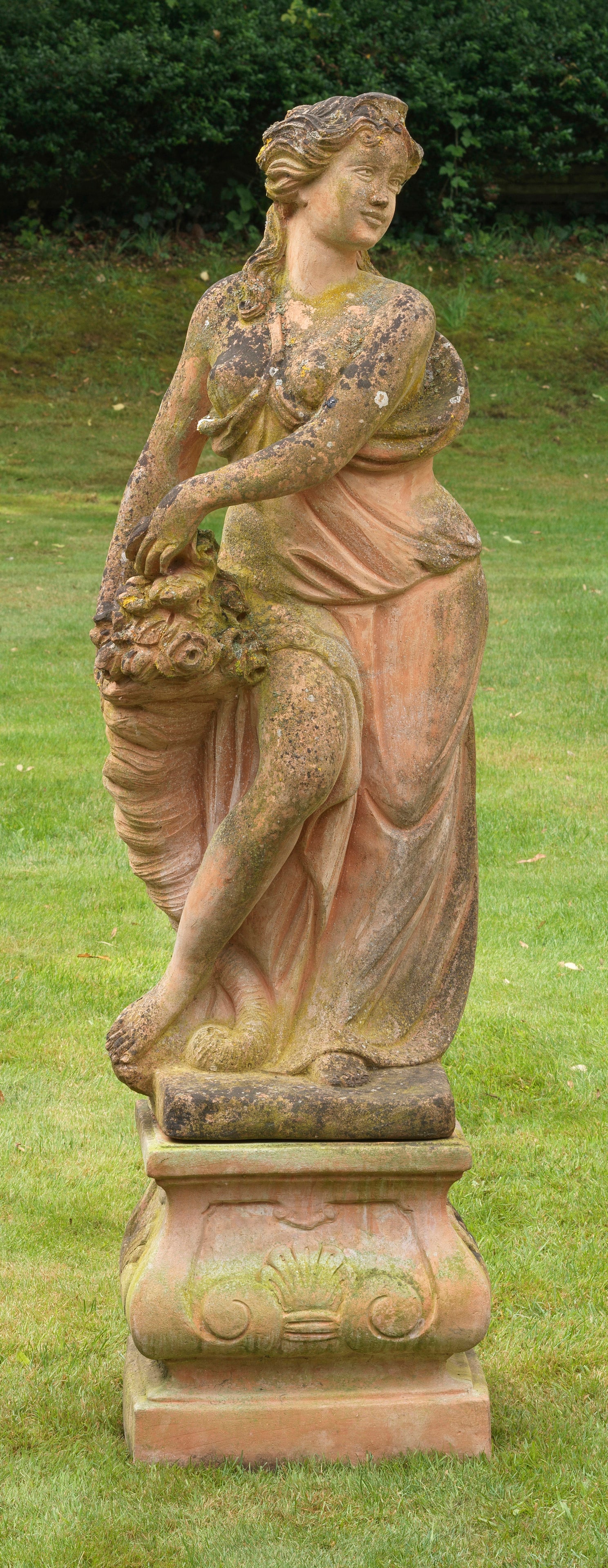 Große Gartenfigur der Flora im Barockstil: Terrakotta, ziegelfarbener Scherben. Auf rechteckig geschweiftem Sockelpodest stehende Göttin Flora, in einen wallenden Mantel gehüllt. Zu ihrer Seite ein Füllhorn mit Rosenblüten stehend. Die bil