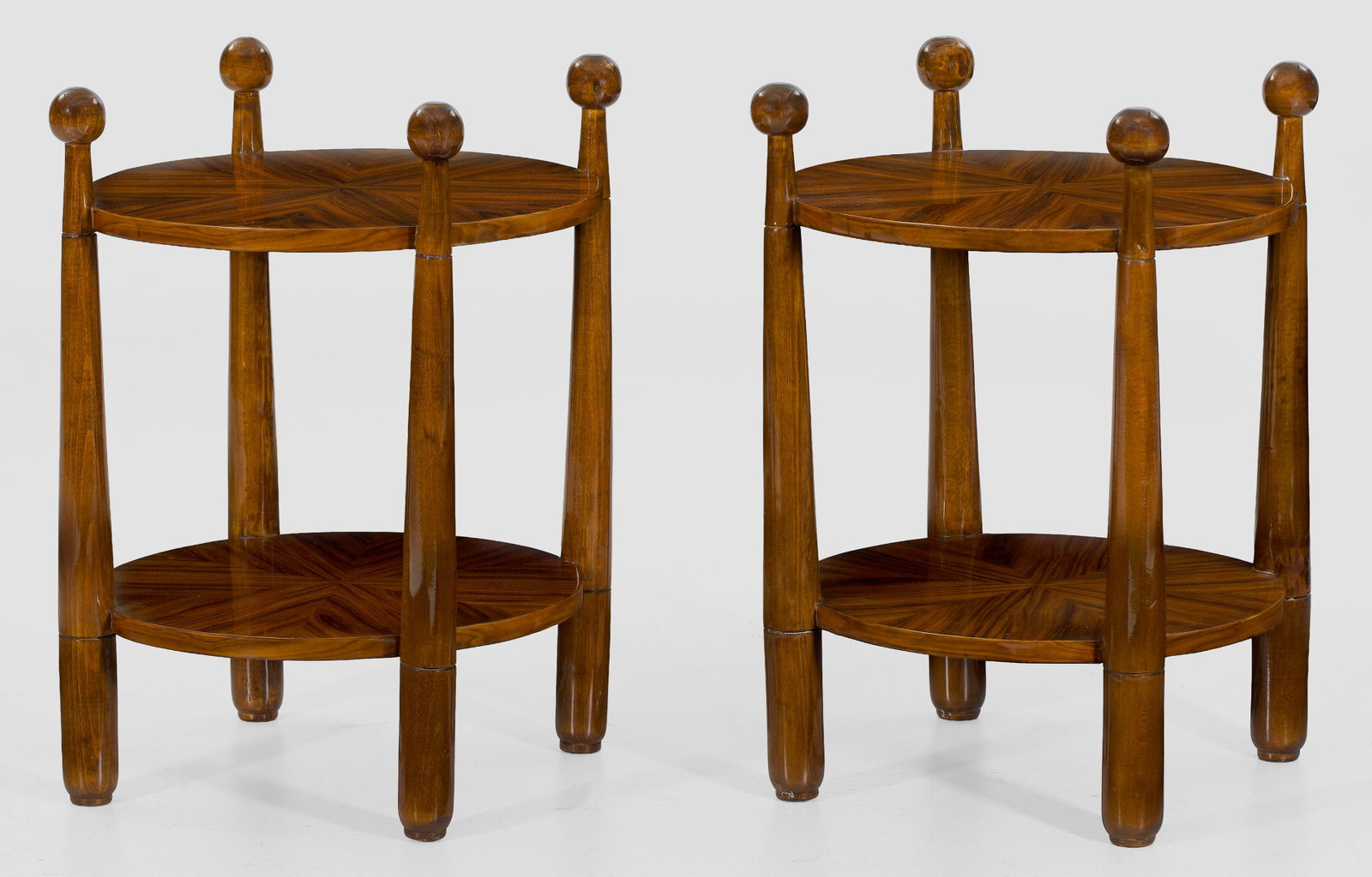 Paar Beistelltische im Art Déco-Stil: Nussbaum, furniert. Sich konisch verjüngende Streben mit Kugelbekrönung als Träger für runde Deckplatte und entsprechendes Ablagefach mit zentriert angeordneten Furnierfeldern. H. 70 cm. D. 57 cmA