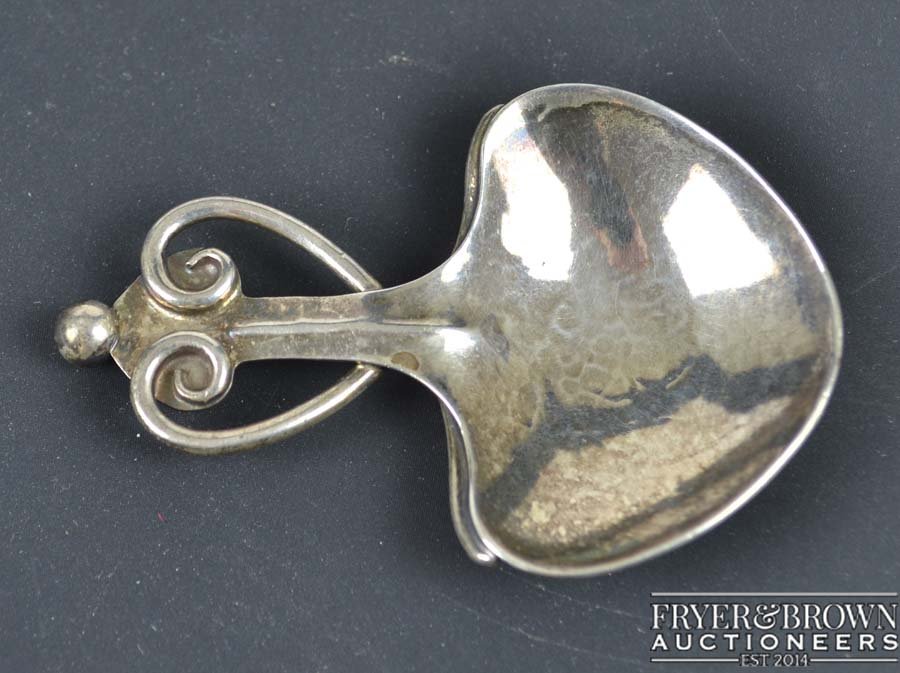 A.E Jones - An Arts and Crafts caddy spoon, the leaf: A.E Jones - An Arts and Crafts caddy spoon, the leaf shaped bowl of planished finish with a scrolled wire heart motif to handle and ball finial, Birmingham 1912, makers mark AEJ within oval, 18grs app