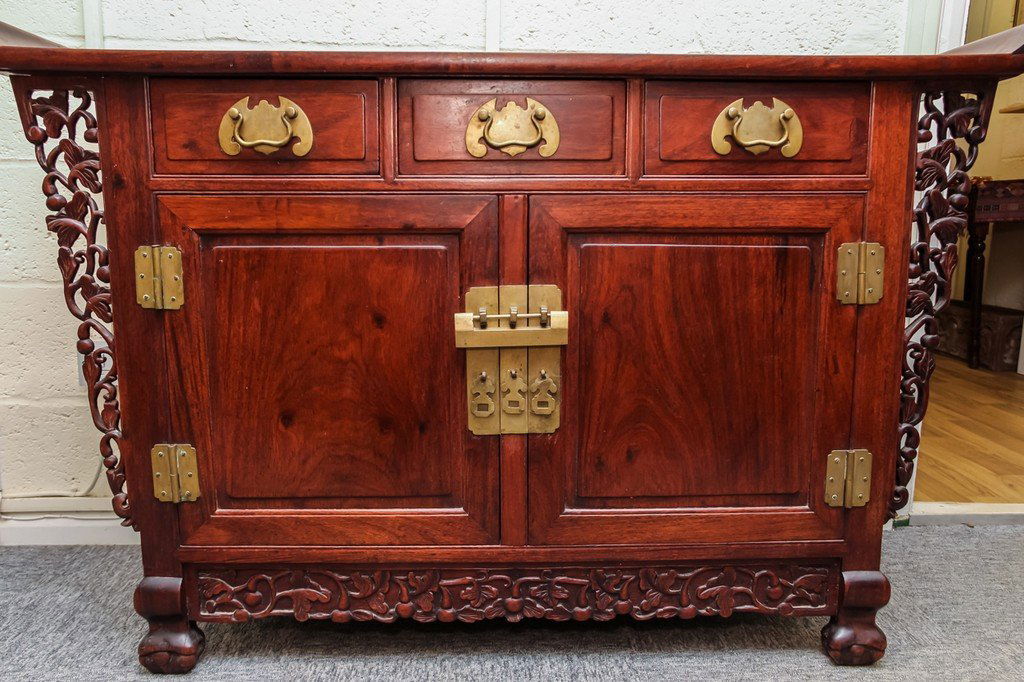 A Chinese hardwood Altar Cabinet with three short: A Chinese hardwood Altar Cabinet with three short drawers over two doors. The rectangular top with curved everted sides, pierced tapering side panels of similar design below on paw feet, brass fitting