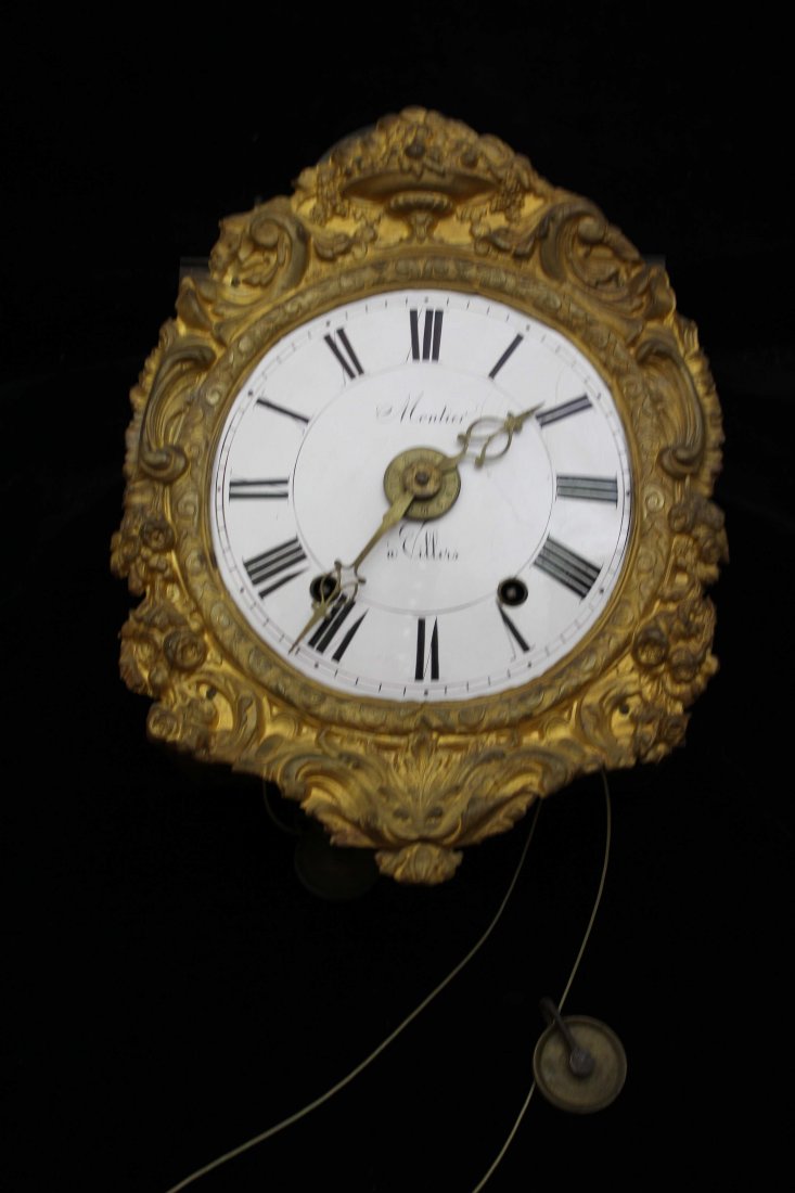 A French pressed metal mounted wall clock, the: A French pressed metal mounted wall clock, the enamelled dial marked Montiers a Villers, encircled by a gilded pressed metal frame of C scrolls beneath a vase with fruit pediment, single large bell to