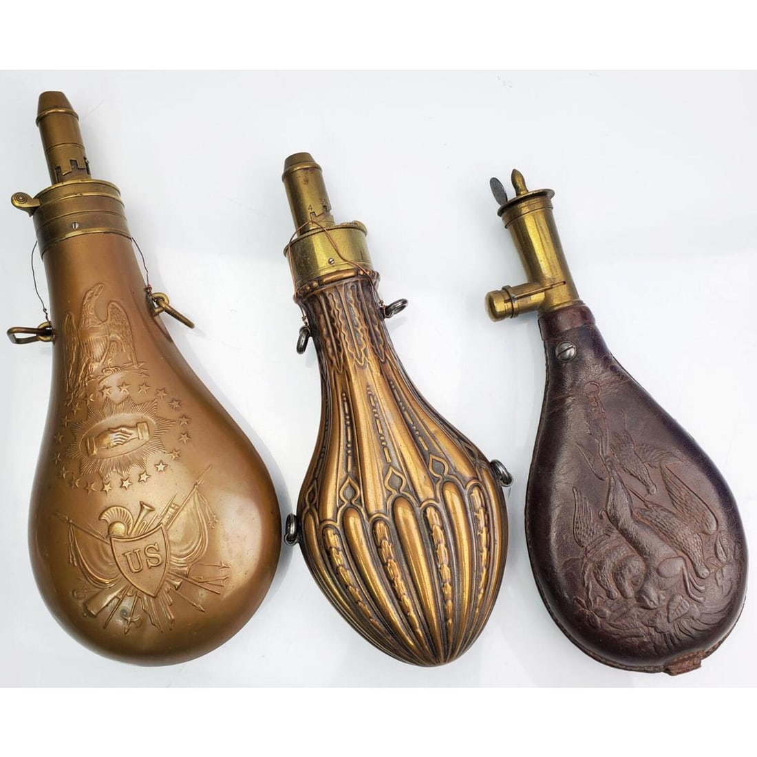 Lot of 3 Antique American Gun Powder Flasks: Lot of 3 Antique American Gun Powder Flasks. 2 Are Copper & Brass. 1 is Embossed Leather. 1 is Marked "Batty" & Dated 1848. Condition: Generally Good. Dimensions: Largest-L-9.5". Provenance: From a Ne