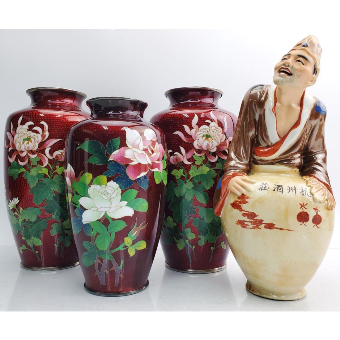 Lot of 3 Japanese Oxblood Cloisonne Vases: Lot of 3 Japanese Oxblood Cloisonne Vases with Silver Rims. Along with a Japanese Male Figure. Condition: Generally Very Good. Dimensions: Each Larger Vase- 8.25" x Dia- 4.5". Provenance: From a Long 