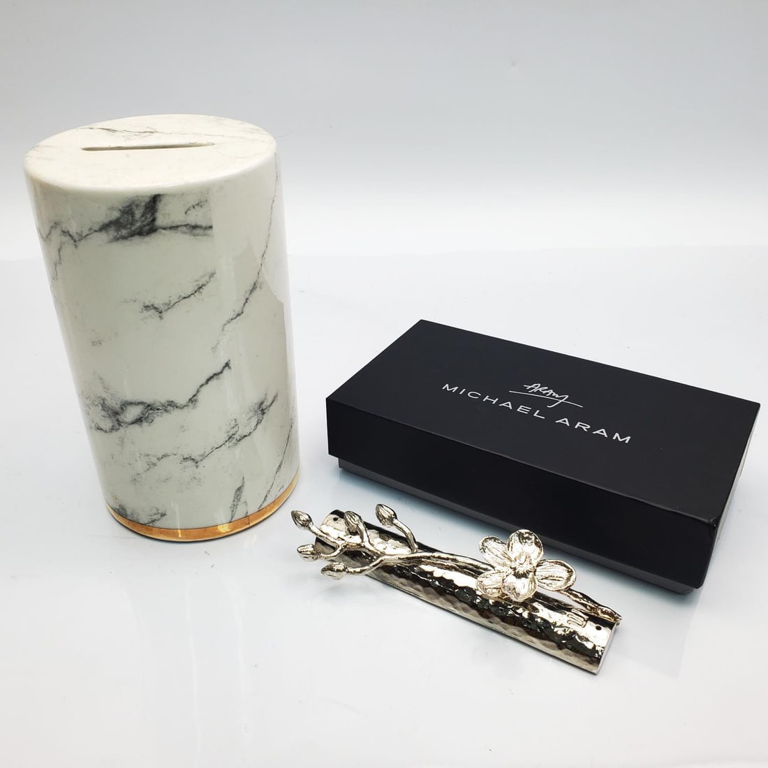 Judaica Michael Aram White Orchid Mezuzah: Judaica Michael Aram White Orchid Mezuzah in Original Box Along w/ a Porcelain Tzedakah Box. Condition: Generally Good. Mezuzah is Unused. Dimensions: Larger H-5.5" x Dia-3.25". Provenance: From a Lon