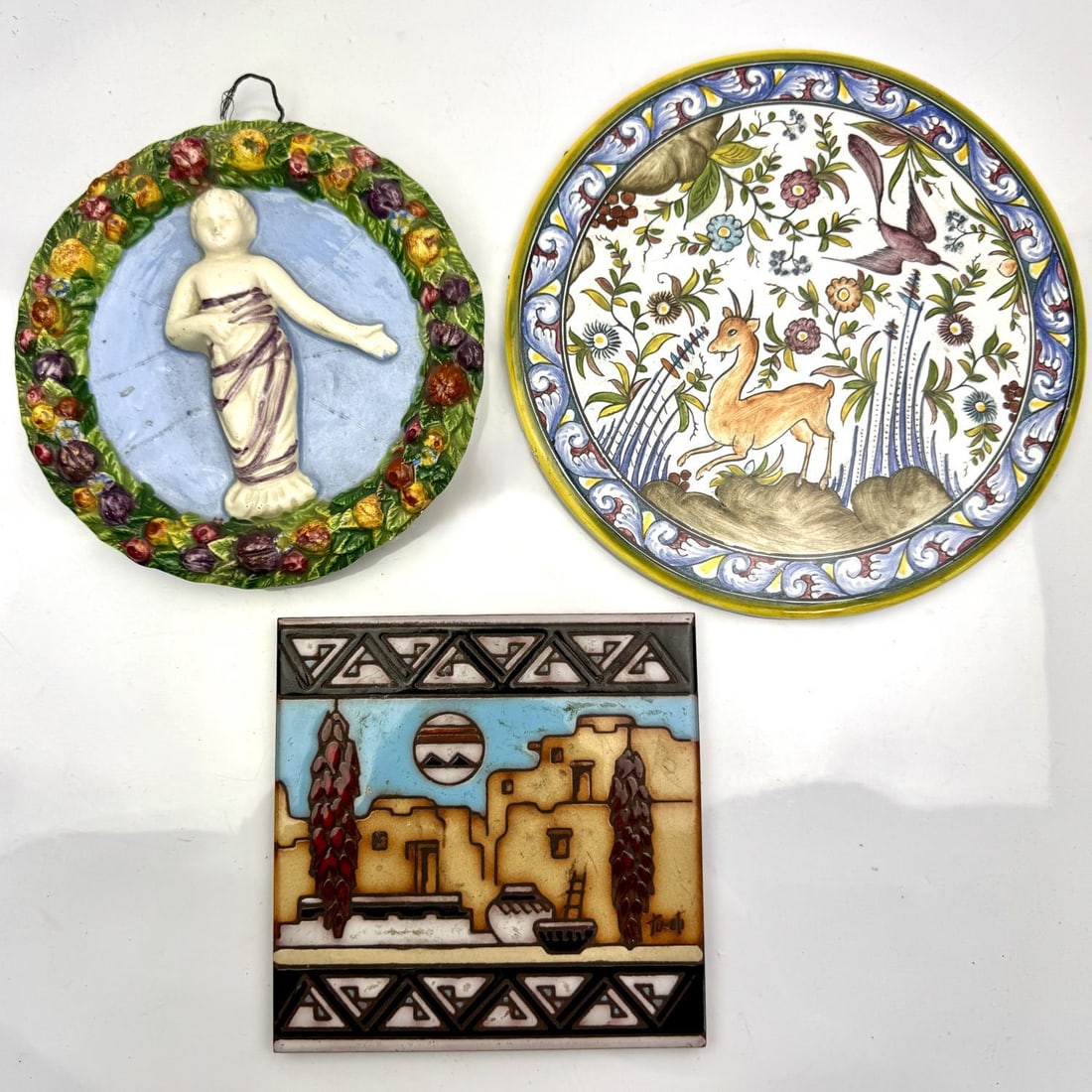 Italian Porcelain Plaque Along w/ a Trivet & Tile: Italian Porcelain Wall Plaque Along with a Trivet and a Ceramic Tile. Condition: Generally Good. The Italian Plaque Has Repairs. All are Sold As Is. Dimensions: Largest Dia (Trivet)- 8.4". Provenance: