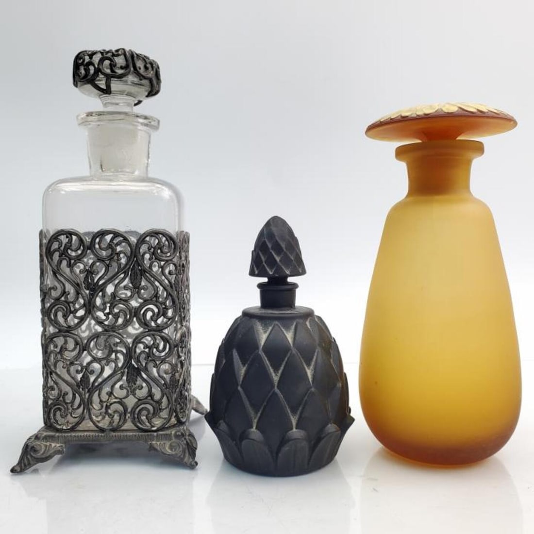 Lot of 2 Antique French Perfume Bottles & Another: Lot of 2 Antique French Perfume Bottles. Along with an Old Metal Mounted Covered Glass Bottle. Perfume Bottles are Circa 1930s. One is Black Glass & One is Yellow Glass w/ a Frozen Sunflower Stopper. 