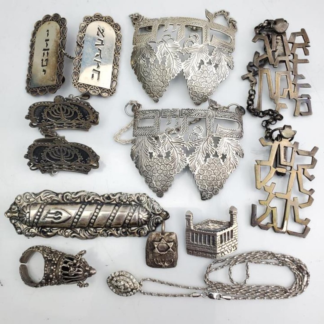 Judaica Group Lot of Silver Items: Judaica Group Lot of Silver Items Including: a Pendant, Large Wine Tags, a Ring, Tallis Clips, a Mezuzah Case & Others. Condition: Generally Very Good. Dimensions: Mezuzah-L-3.5". Gross Weight: 182.7g