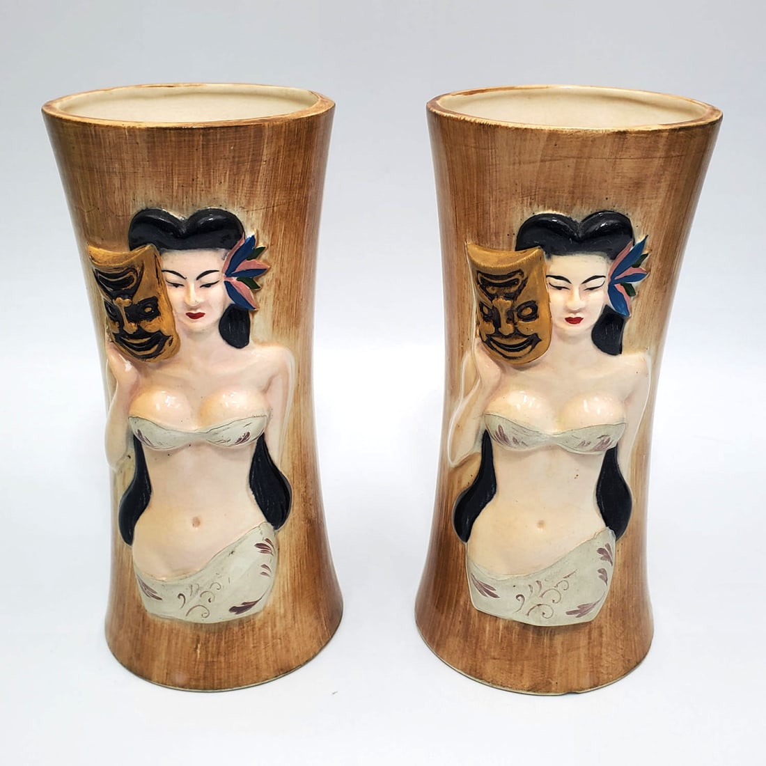 Pair of Vintage Hawaii Kai Hula Girl Mugs: Pair of Vintage Hawaii Kai Hula Girl w/ Tii Mask Mugs. Fully Signed. Condition: Generally Good. 1 Has a Chip on The Bottom. Dimensions: H- 7" x Dia- 3.25". Provenance: From a Long Island, NY Estate.
