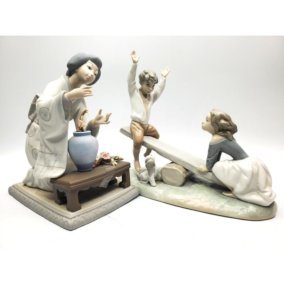 Lot of 2 Vintage Lladro Porcelain Figures: Lot of 2 Vintage Lladro Porcelain Figures Including "Kids on a Seesaw" & "Geisha w/ Flowers". Both are Fully Marked. Condition: Seesaw is in Generally Good Condition. The Geisha Flowers Are Chipped. D