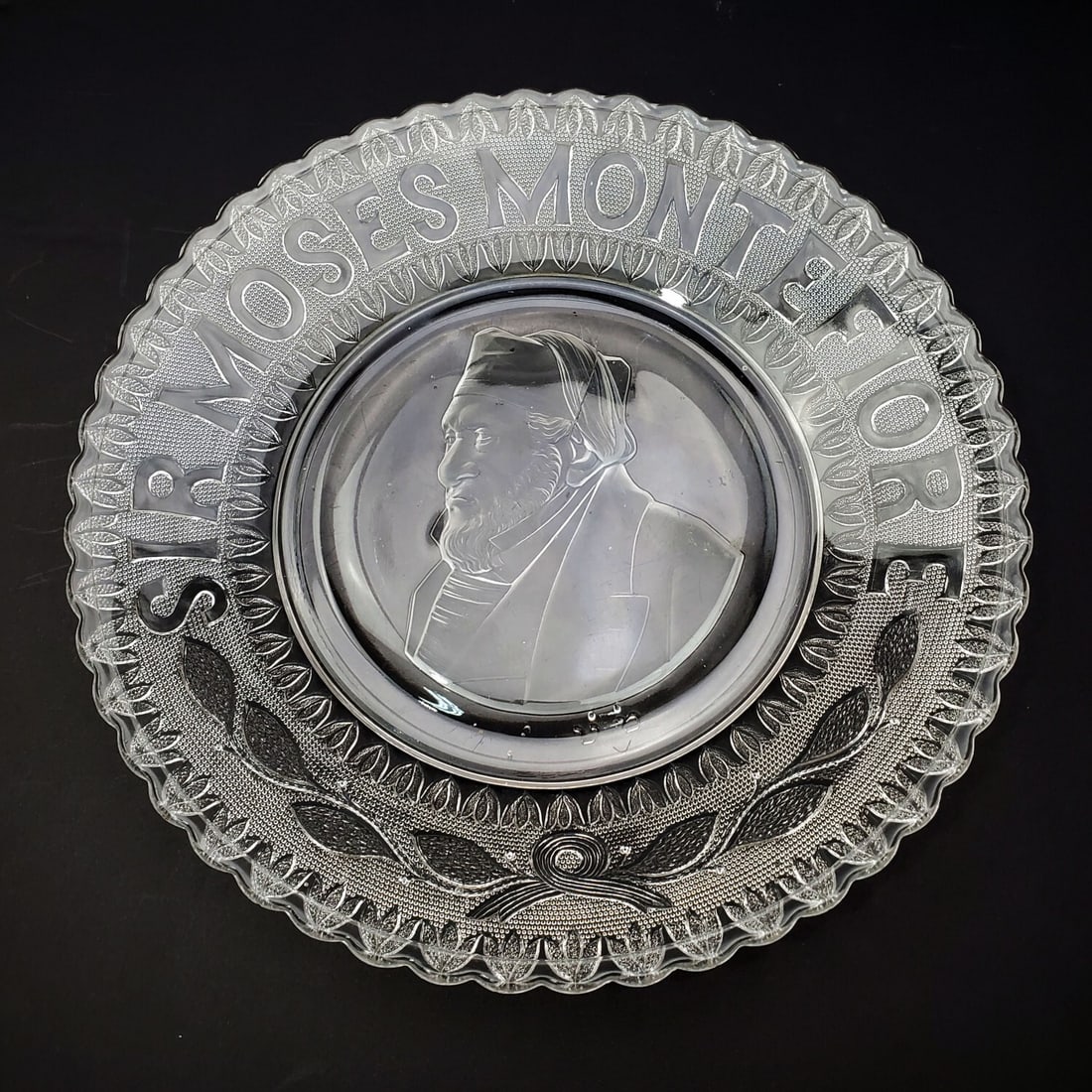 Judaica Antique Commemorative Plate Montefiore: Judaica Antique Glass Commemorative Plate Portraying Sir Moses Montefiore. c.1880's. Condition: Generally Good w/ a Scratch on the Surface. Dimensions: Larger-Dia-10.5". Provenance: From a Long Island
