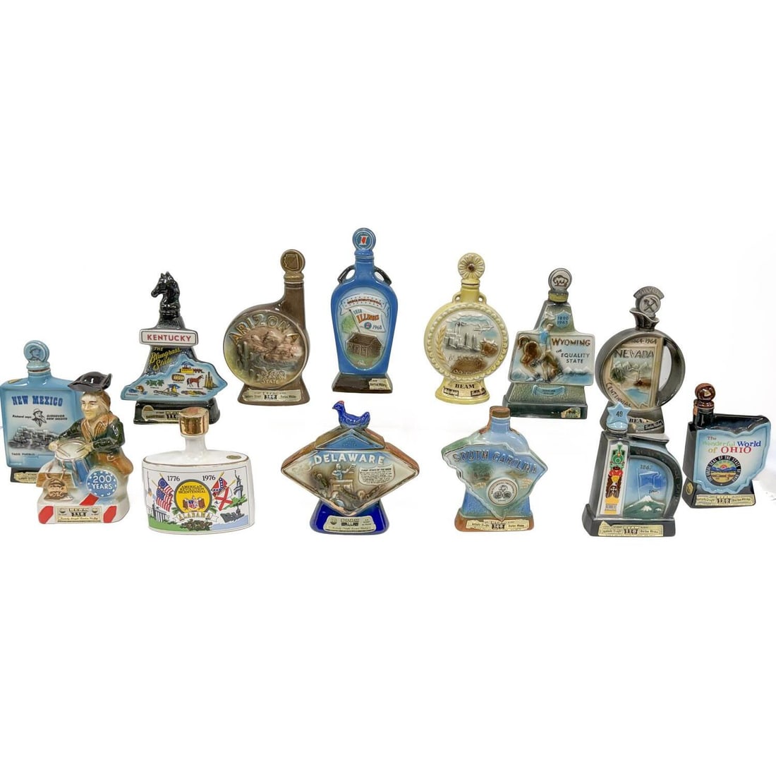 13Jim Bean State Porcelain Empty Decanters: Lot of 13 Jim Bean State Porcelain Empty Decanters Including Alabama (1976), Alaska (1967), Arizona (1968), Delaware (1972), Illinois (1968), Kansas (1960), Kentucky (1967), New Mexico (1968), Ohio (1