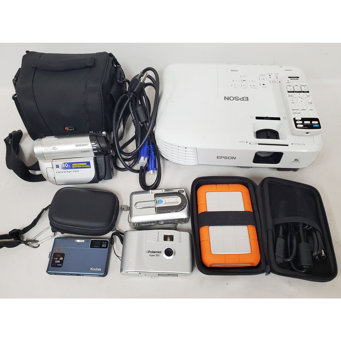 Epson VS250 3LCD Projector, & Others: Epson VS250 3LCD Projector Along w/ 1 RCA VHS Camcorder in Original Case, 1 Sony Handycam in Original Case, & Others. Condition: As Found. Projector Appears to be Unused. Please Note- We Do Not Guaran