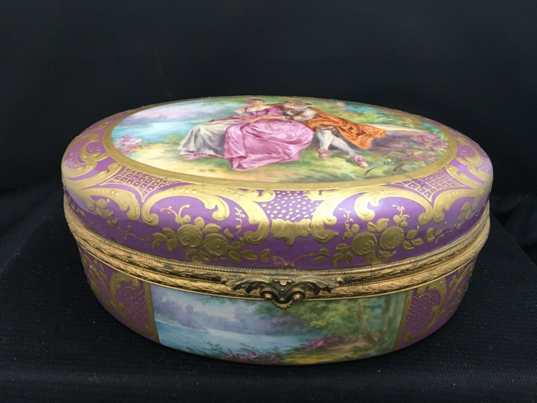 Sèvres Style Oval-Shaped Portrait Box: Lavender oval-shaped box with gilded designs and very vibrant and colorful portrait of nobleman and noblewoman sitting in nature. Openable, with floral designs on white interior.7.5” x 5.5”