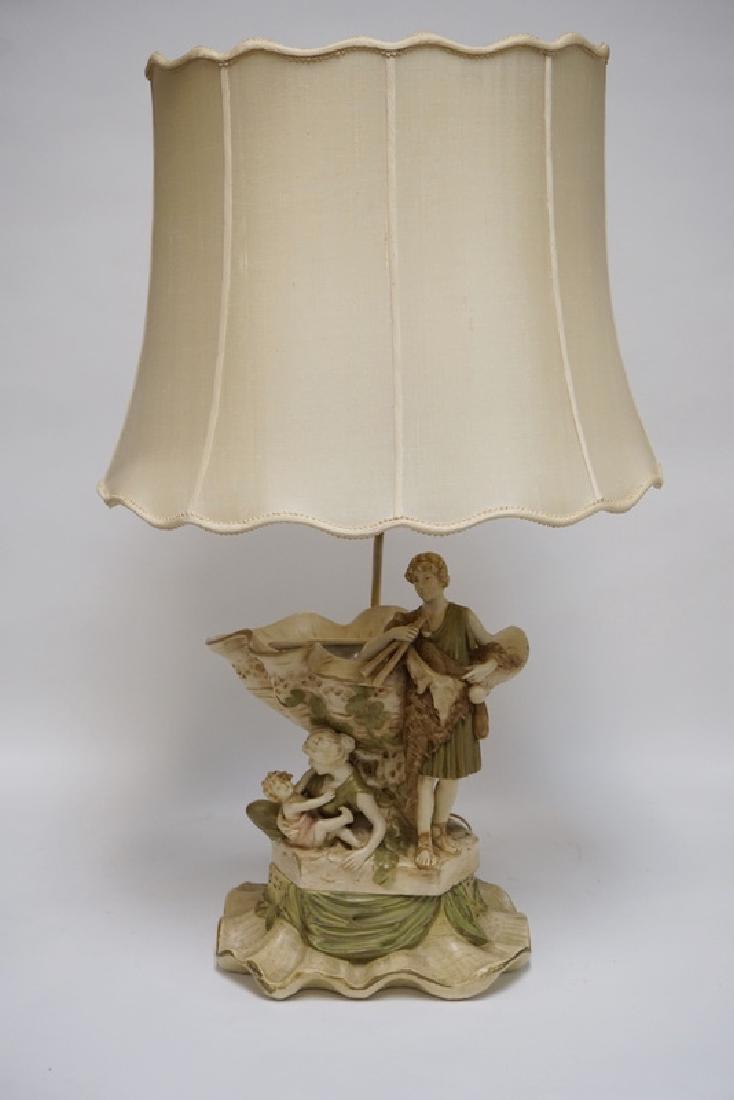 ROYAL DUX TABLE LAMP IN THE FORM OF A MAN WITH FLUTES: ROYAL DUX TABLE LAMP IN THE FORM OF A MAN WITH FLUTES AND A RECLINING WOMAN HOLDING A CHILD. 35 INCHES HIGH OVERALL. AS MOUNTED THERE IS NO VISIBLE MARK. WE ARE ATTRIBUTING THIS TO ROYAL DUX.
