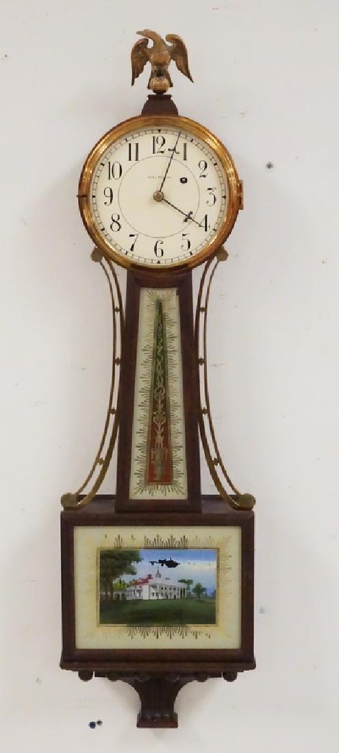 WALTHAM BANJO CLOCK: WALTHAM BANJO CLOCK WITH REVERSE PAINTED PANELS AND AN EAGLE FINIAL. 37 1/2 INCHES LONG. 10 1/4 INCHES WIDE. MISSING GLASS OVER FACE.