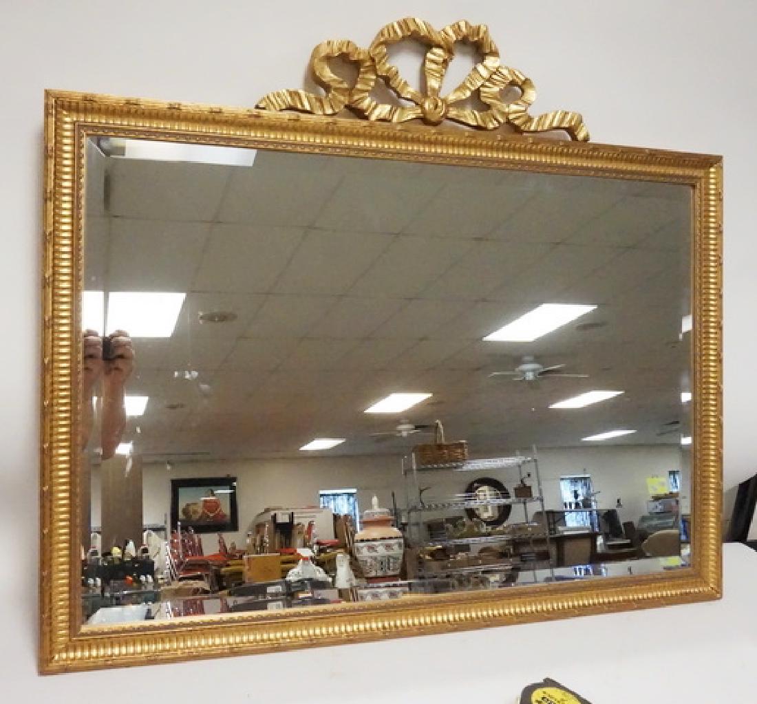 GILT BEVELED MIRROR: BEVELED MIRROR IN GILT FRAME WITH BOW CREST. DAISY FUENTES 39 1/2 IN X 33 1/2 IN OVERALL