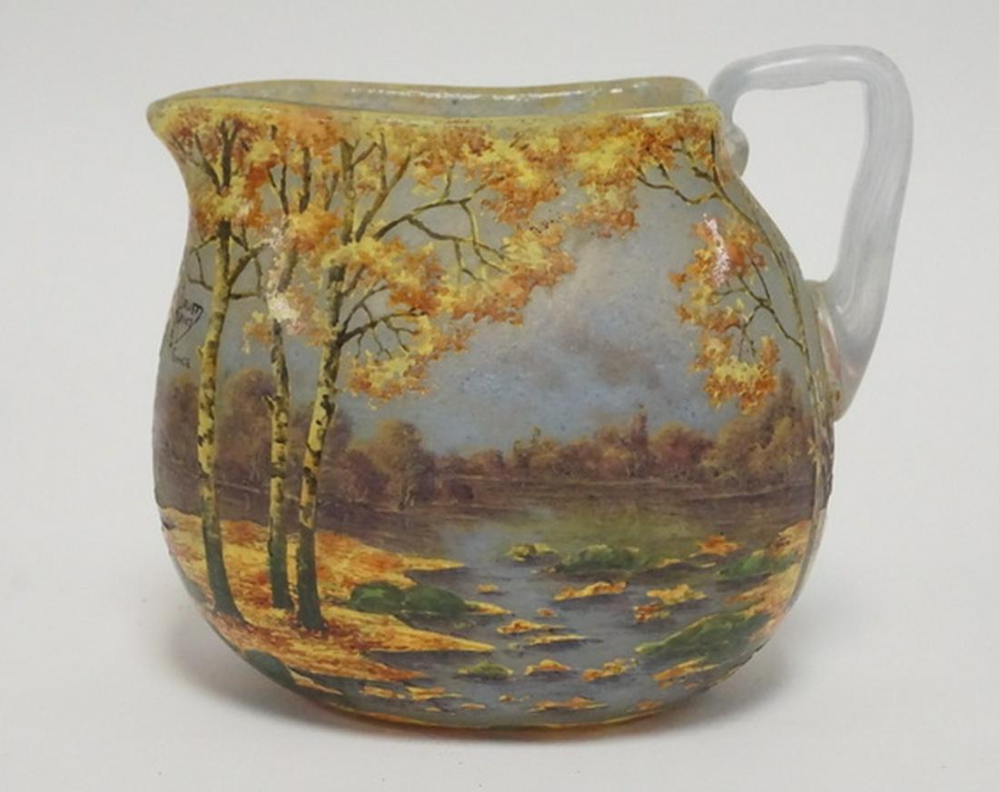 DAUM NANCY CAMEO CUTBACK PITCHER: DAUM NANCY CAMEO CUT GLASS PITCHER. DECORATED WITH A VIBRANT AUTUMN LANDSCAPE FEATURING TREES AND A LAKE. 5 1/2 INCHES HIGH. HANDLE HAS A CRACK AT AT THE TOP WHERE IT IS APPLED.