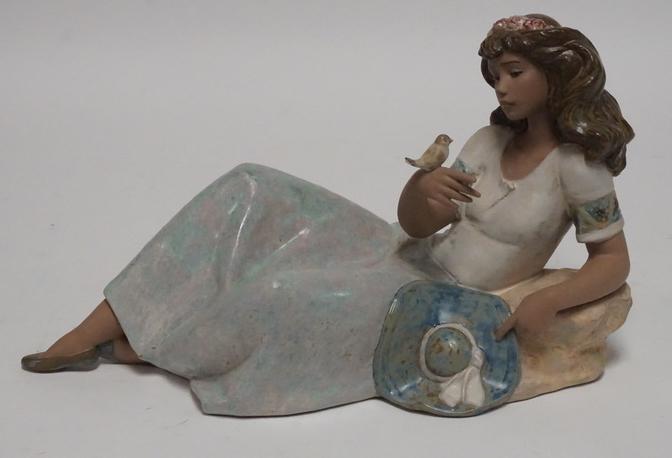 LLADRO: LLADRO PORCELAIN FIGURE OF A RECLINING WOMAN WITH A BIRD PERCHED ON HER HAND. 7 3/4 INCHES HIGH. 13 1/2 INCHES LONG.