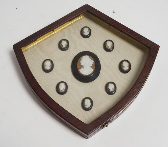 SET OF CARVED CAMEO MEDALLIONS IN A SHADOWBOX FRAME: SET OF 9 CARVED CAMEO MEDALLIONS MOUNTED IN A SHIELD SHAPED SHADOW BOX FRAME. 10 X 9 1/4 INCHES.