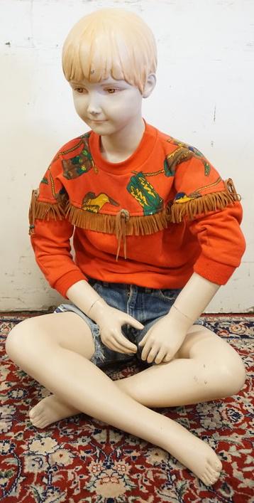 MALE MANNEQUIN CLOTHED WITH VINTAGE SELVEDGE JEANS: MALE MANNEQUIN CLOTHED WITH VINTAGE SELVEDGE JEANS THAT ARE CUT OFF INTO SHORTS, VINTAGE MILTON FUN WEAR FRINGED PULL OVER SHIRT AND WESTERN BEADED BELT. SEATED MANNEQUIN IS APPROXIMATELY 30 IN TALL. 