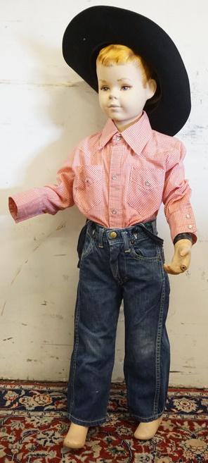 YOUNG BOY MANNEQUIN CLOTHED WITH LEE JEANS: YOUNG BOY MANNEQUIN CLOTHED WITH LEE JEANS , JEAN SUSPENDERS, VINTAGE TRUE WEST ROCKMOUNT RANCH WEAR SHIRT AND COWBOY HAT WITH FEATHERS AND MOWGLI PIN. MANNEQUIN MISSING AN ARM AND FINGER AND IS APPRO