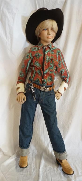BOY MANNEQUIN CLOTHED IN LEVIS JEANS & WESTERN ATTIRE: BOY MANNEQUIN CLOTHED IN LEVIS JEANS, COWBOY BOOTS, BELT W/ BELT BUCKLE, VINTAGE STIR-UPS WESTER SHIRT, BOLLO TIE W/ TIE CLIP, ARM BANDS, & A TRAIL BOSS COWBOY HAT. APP. 52 IN TALL. MANNEQUIN MAY SUFF